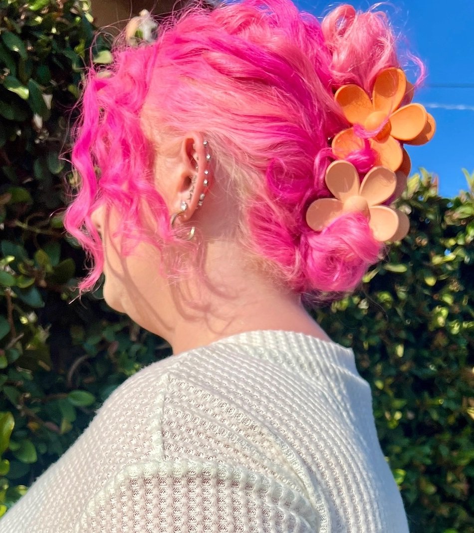 Bright pink textured low bun with loose curls and flower clips