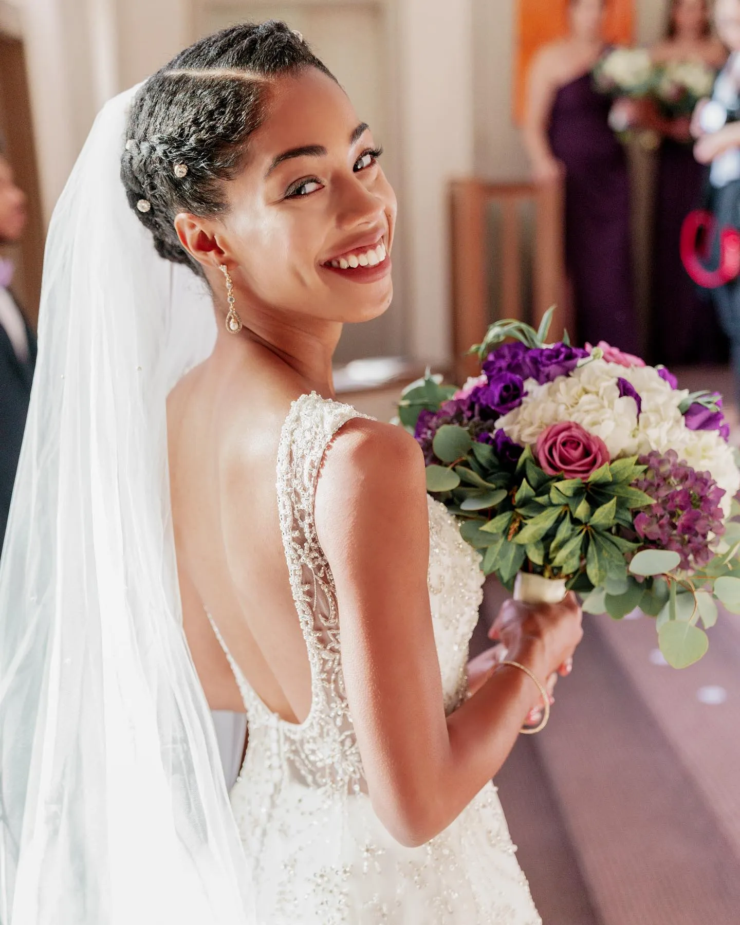 Braided low bridal updo with smooth side sections, pearl pins and a veil