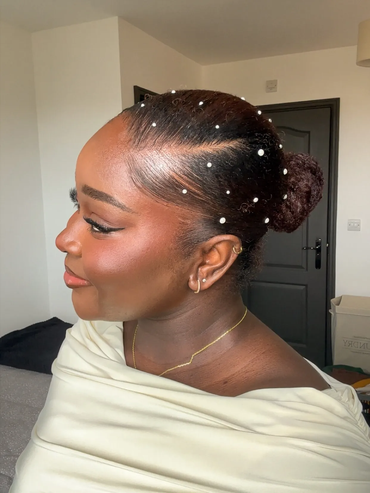 Sleek low bridal bun with smooth side part and scattered pearl pins