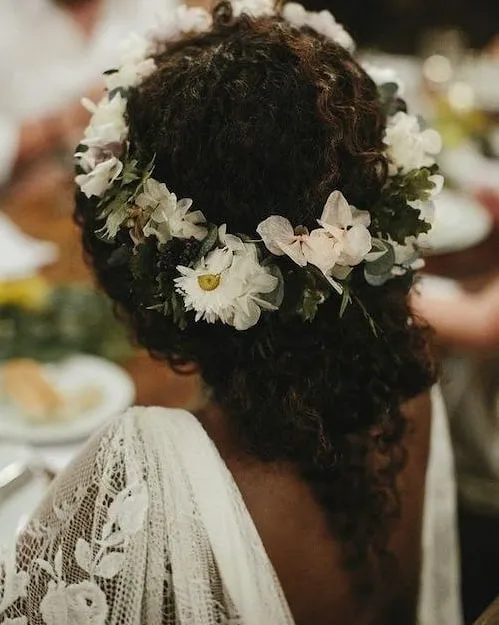 Low textured bridal updo with white flower crown and loose curled tendril