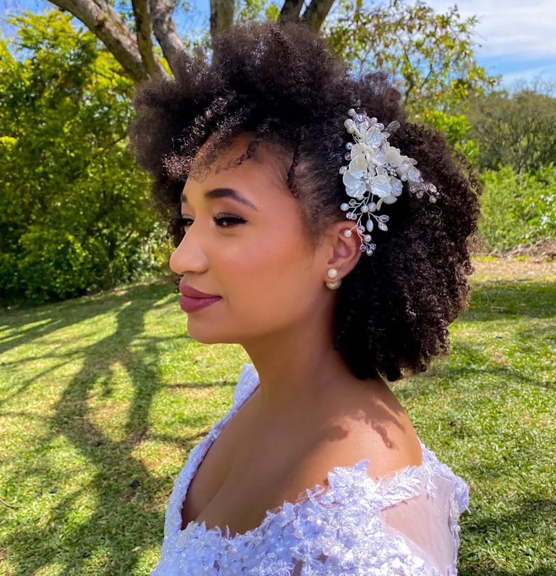 Voluminous side-swept Afro bridal hairstyle with white floral hair clip