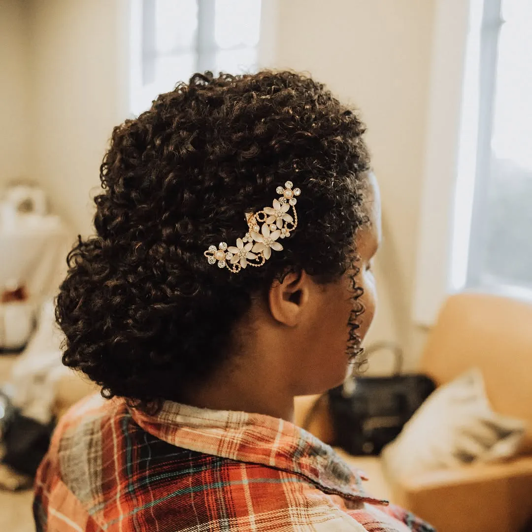 Rounded curly bridal updo with compact curls and a gold leaf hair comb