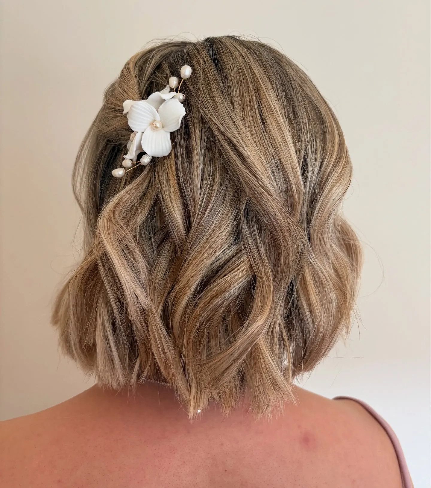 Wavy blonde bob with a white flower and pearl hair accessory