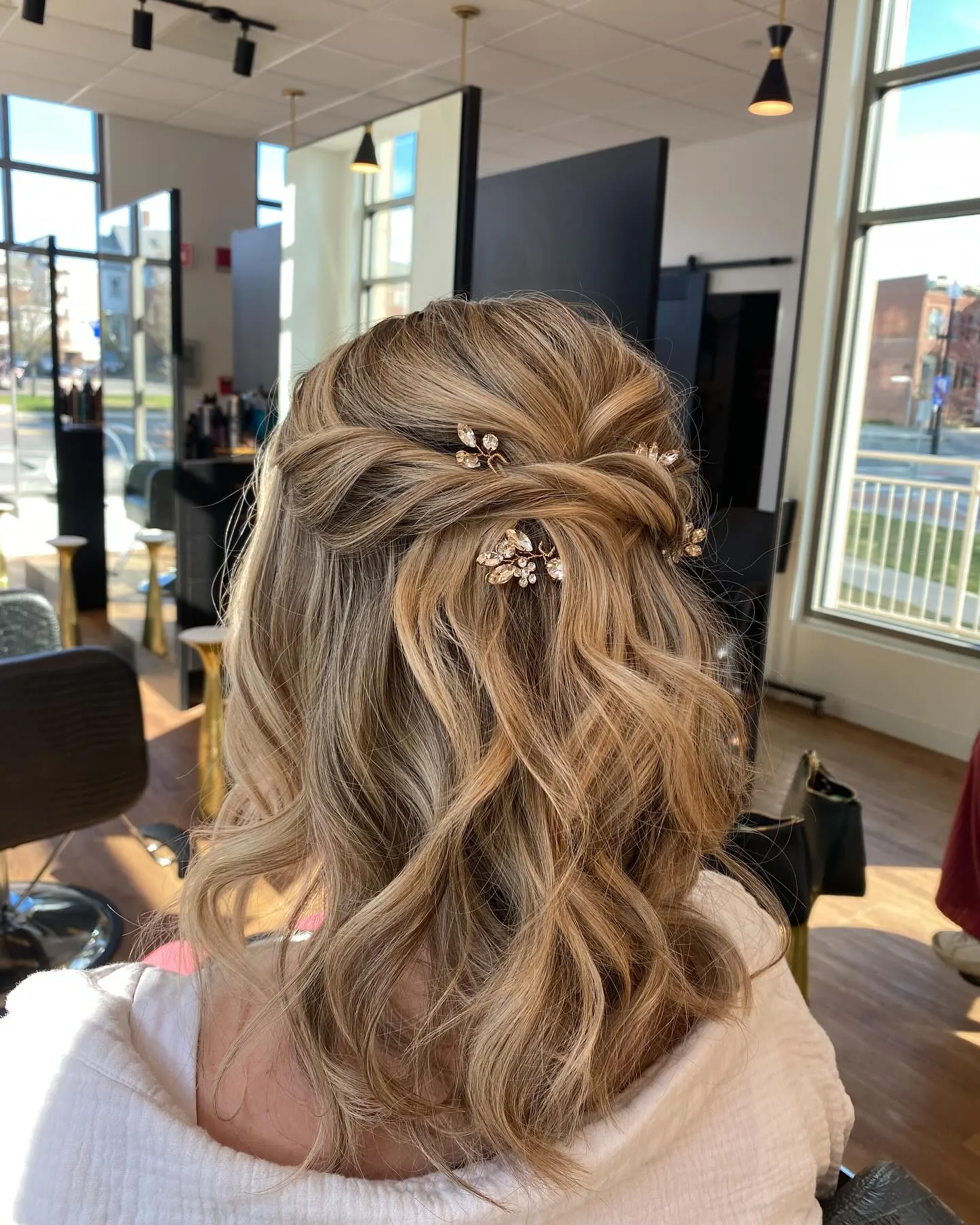 Twisted half-up hairstyle with soft shoulder-length waves and small gold pins
