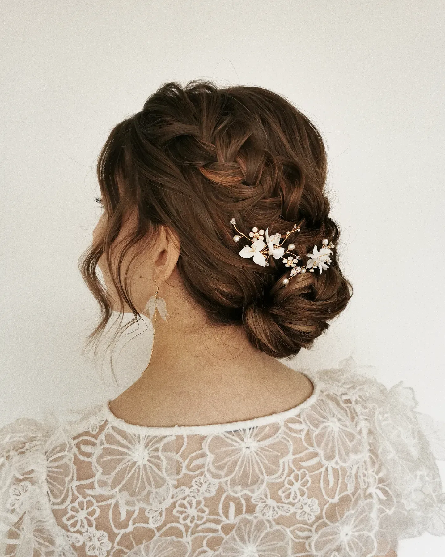 Textured low bridal bun with loose face-framing pieces and white floral pins