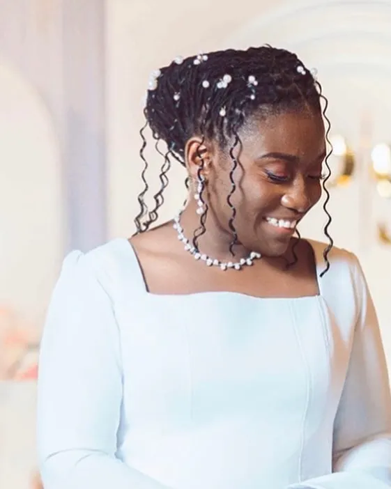 Braided bridal updo with pearl accents and loose spiral tendrils