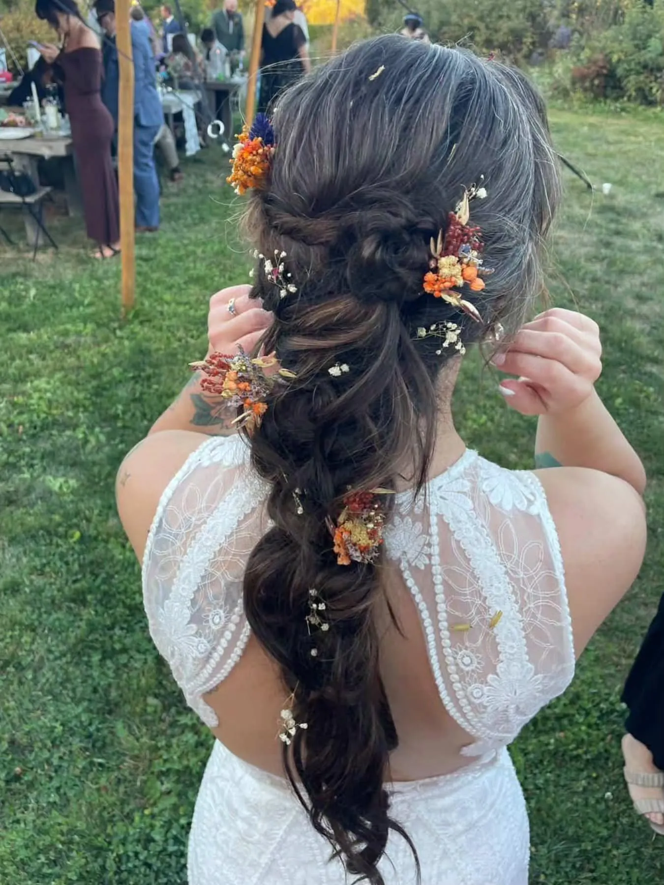 Textured low boho bridal braid with scattered orange and white flowers