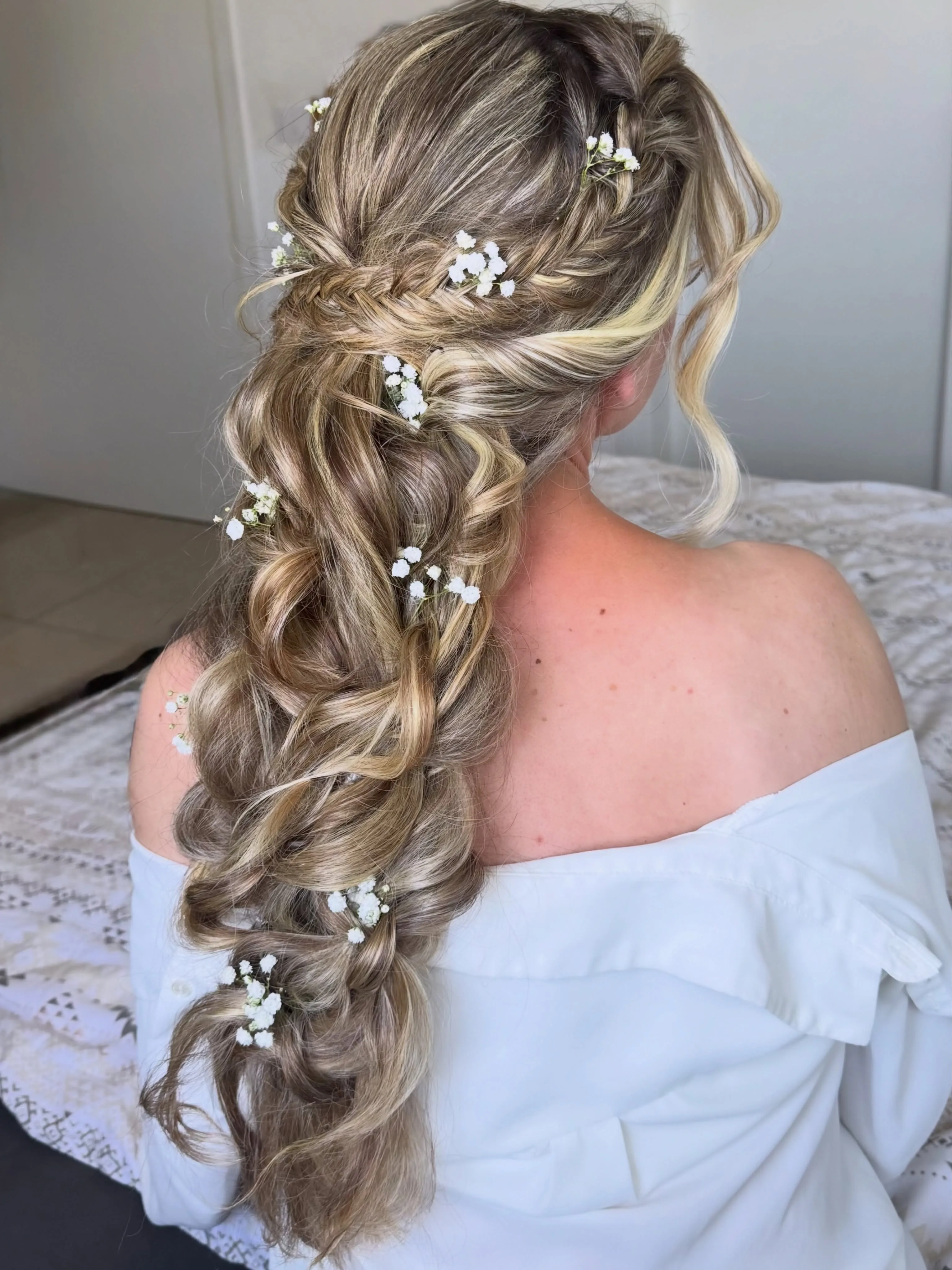 Voluminous side boho bridal braid with loose face-framing pieces and tiny flowers
