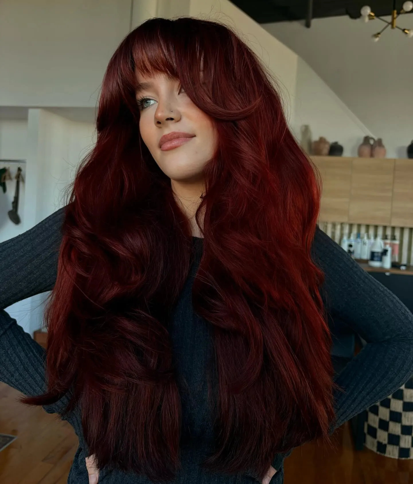 Long red layered hair with full curtain bangs and soft waves