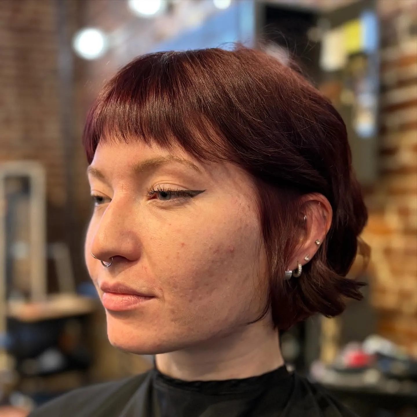 Short cropped haircut with a blunt micro fringe in a muted red tone