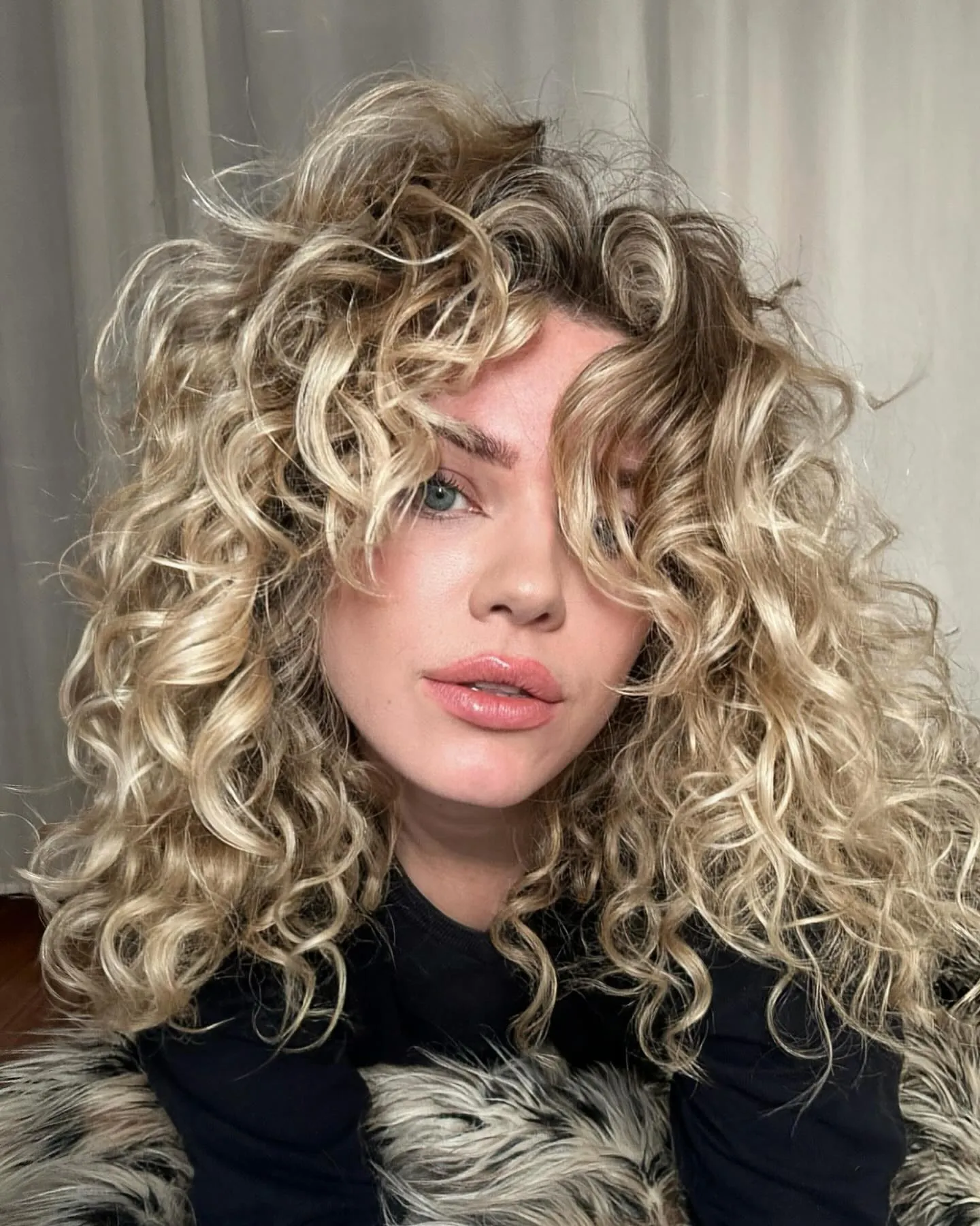 Shoulder-length blonde spiral curls with a center part
