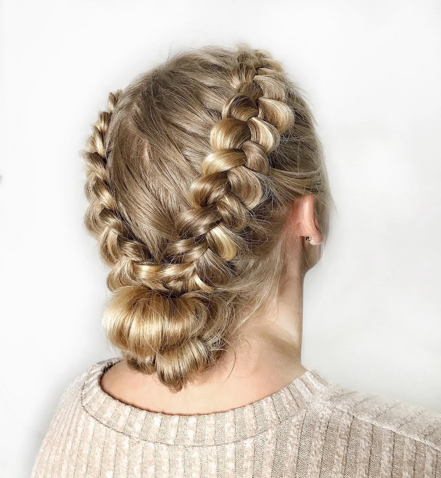 Long blonde hair styled in two braids leading into a low bun