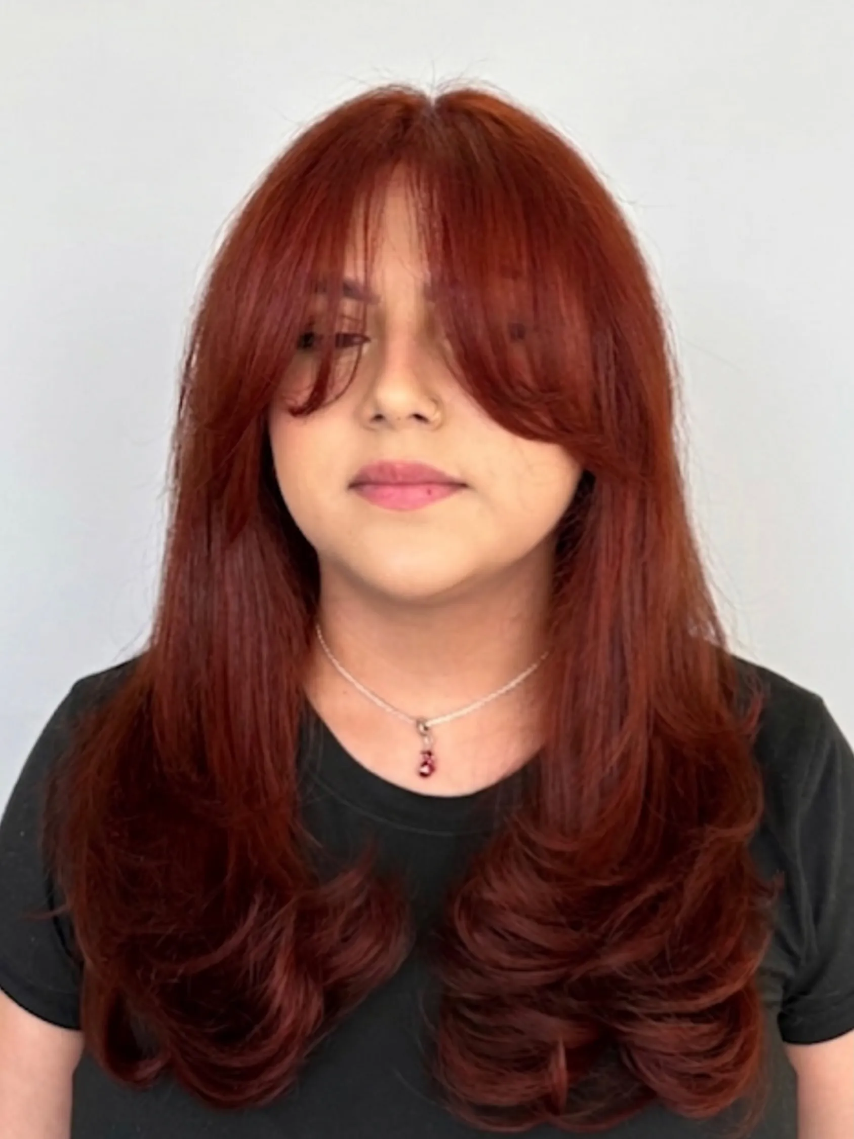 Long red layered hair with curtain bangs and curved ends