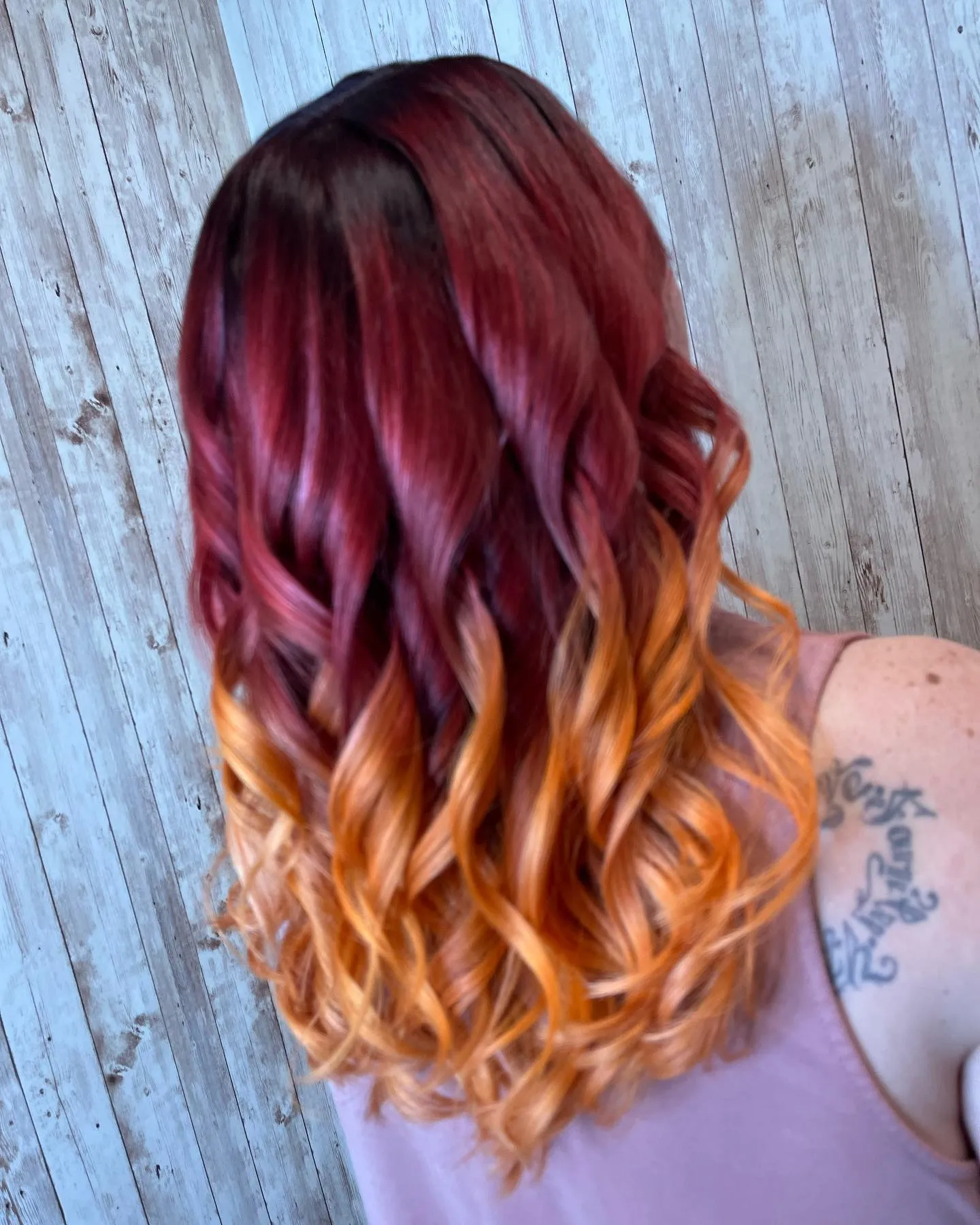Medium-length curls fading from burgundy roots into orange ends