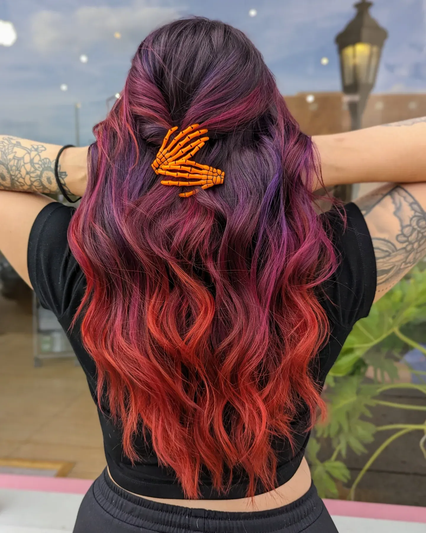 Long red and purple waves styled half-up with an orange hair clip