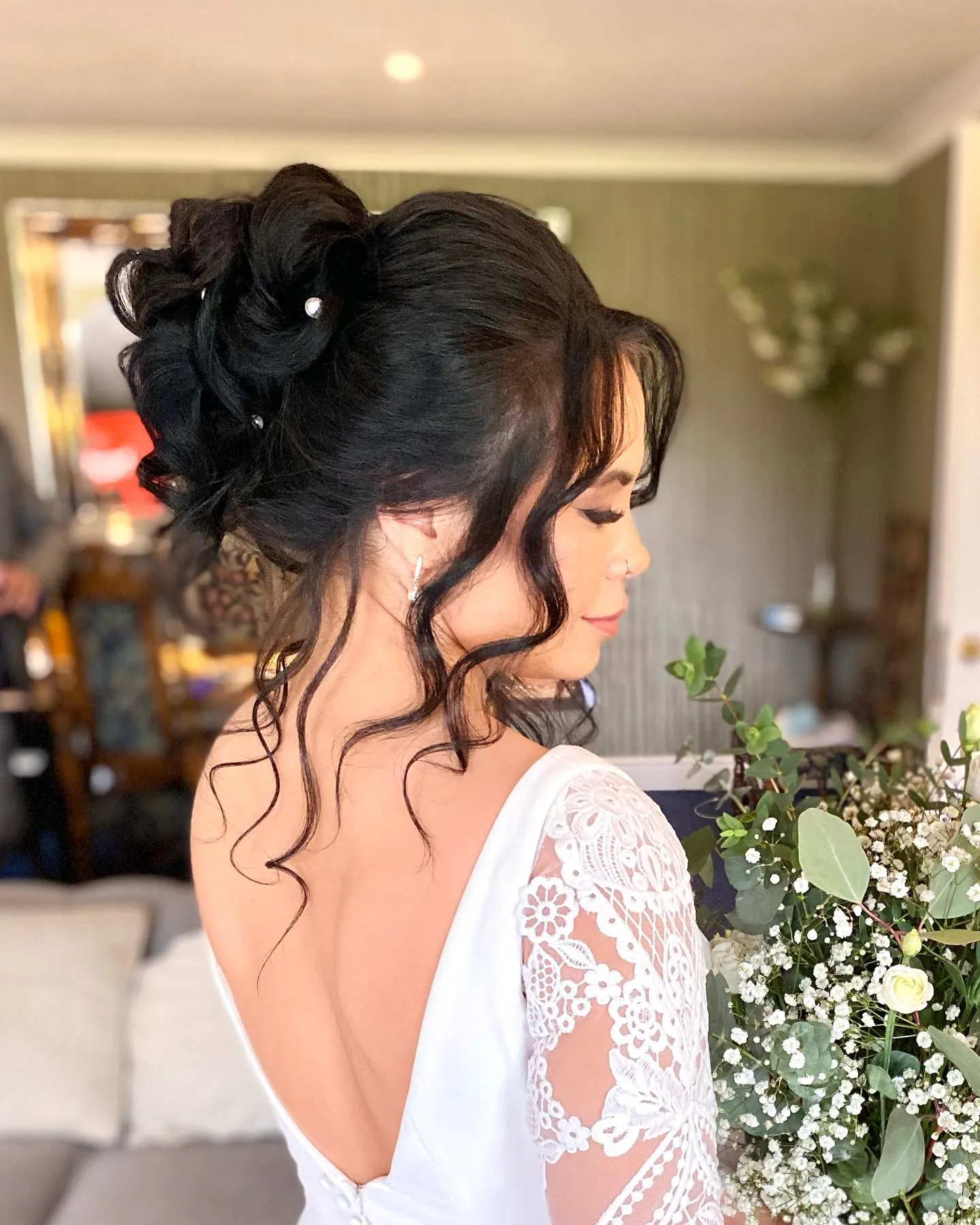 Loose dark high bun with pearl pins and curled face-framing tendrils