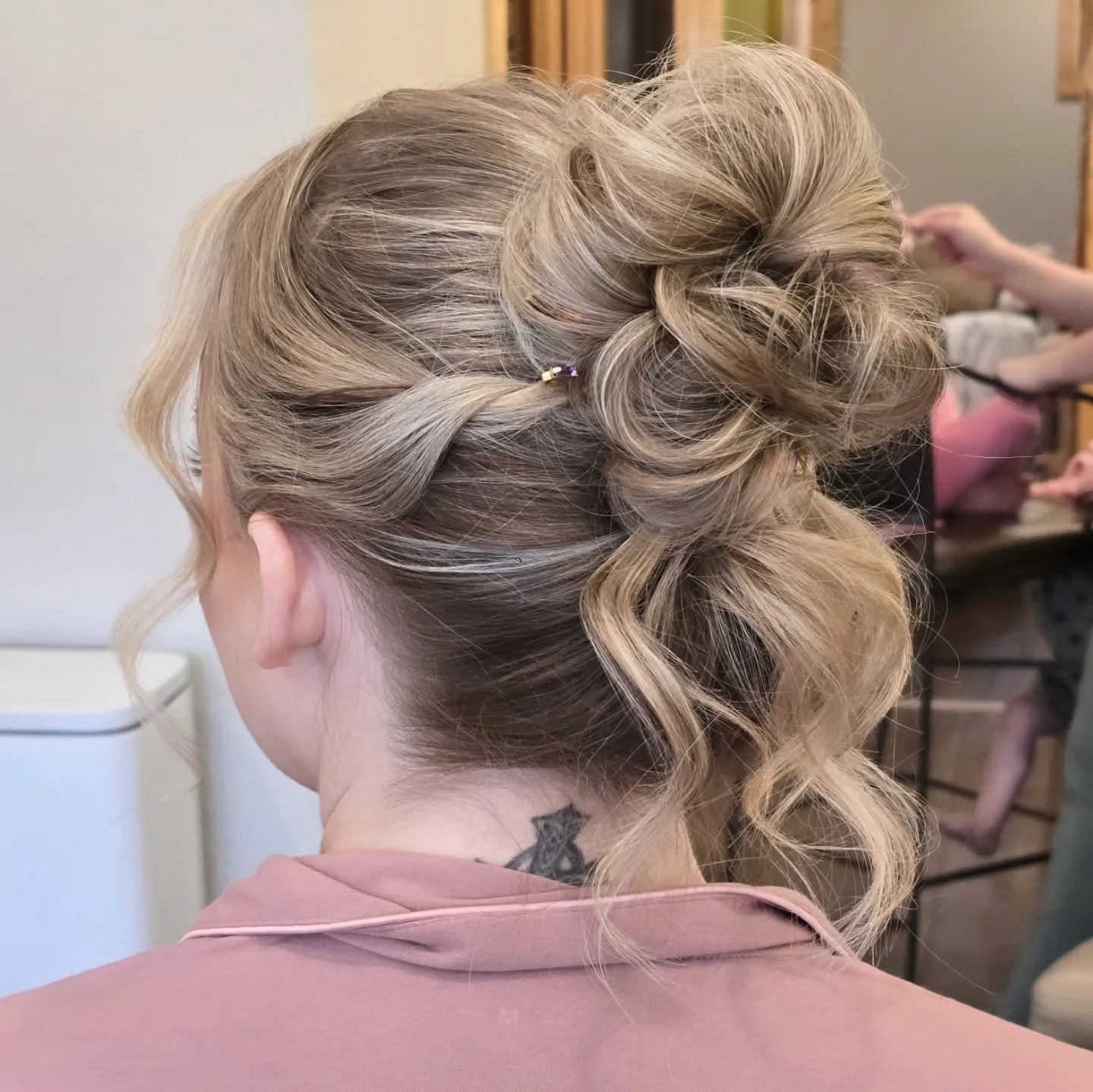 Braided blonde high bun with pearl detail and a loose curled section at the nape