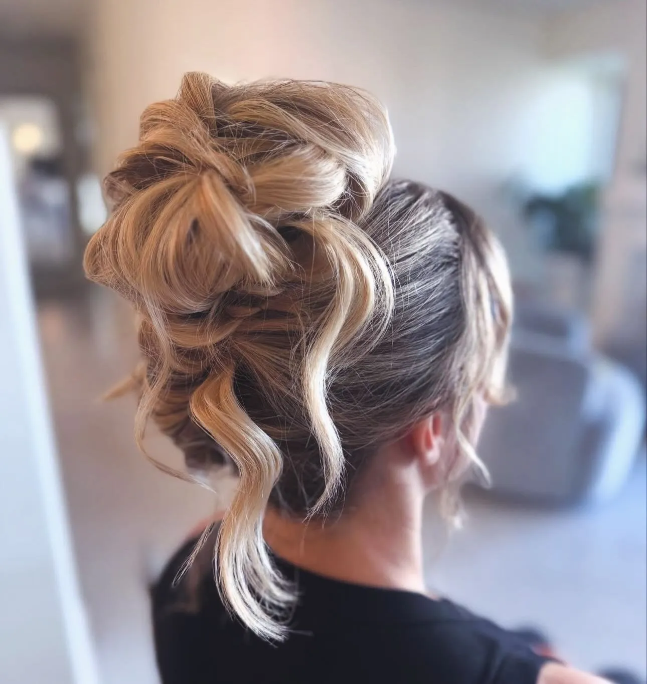 Loose blonde curled high bun with long draped pieces and soft face framing