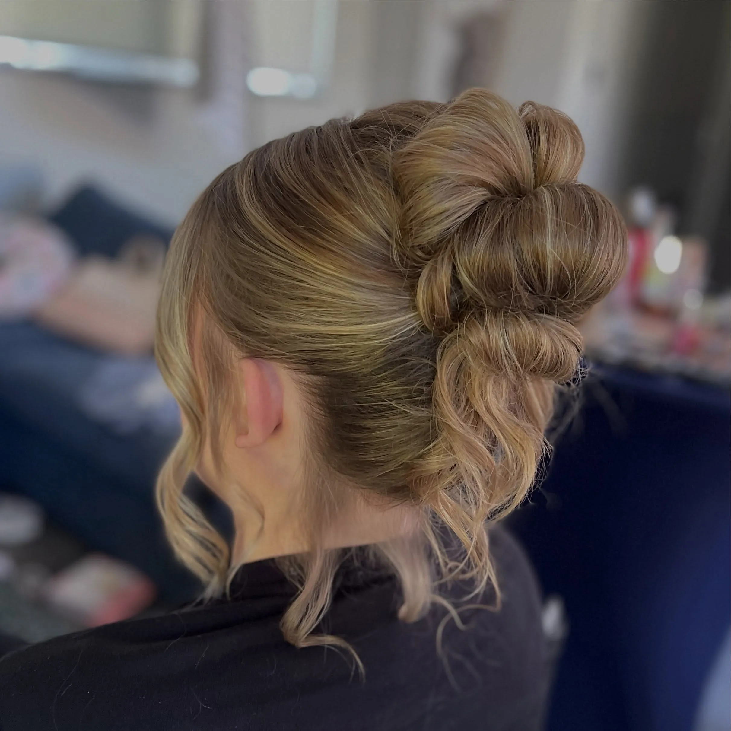 Looped blonde high bun with large folded sections and long curled tendrils