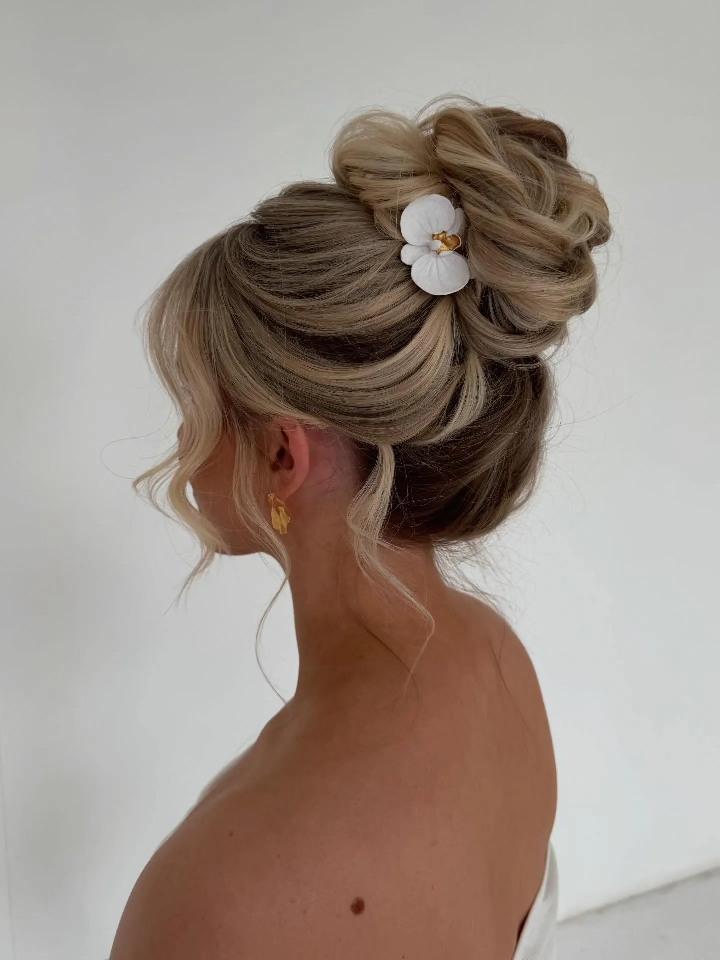 Blonde twisted high bun with a white flower clip and soft side pieces