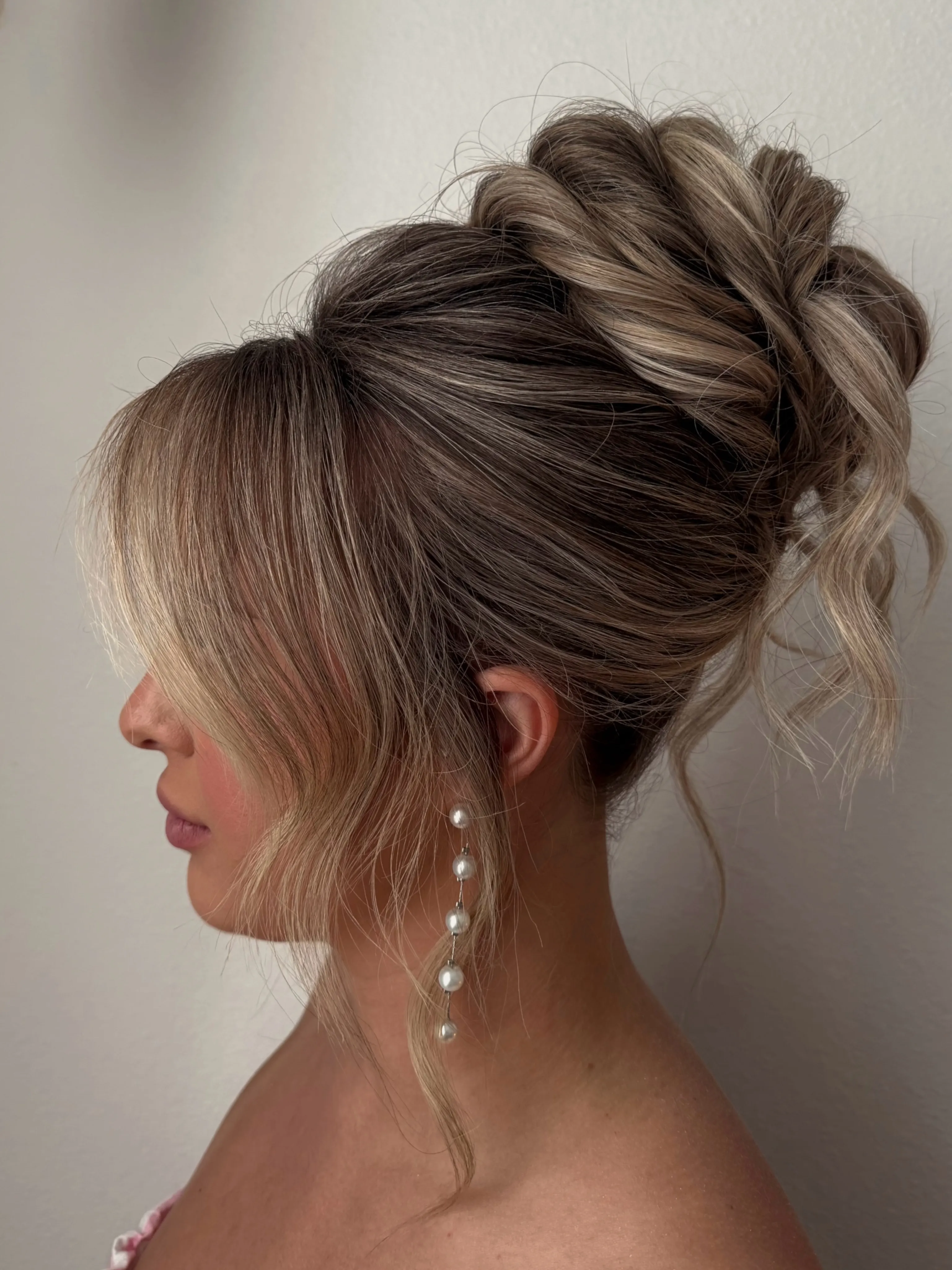 Textured blonde high bun with wispy curled tendrils