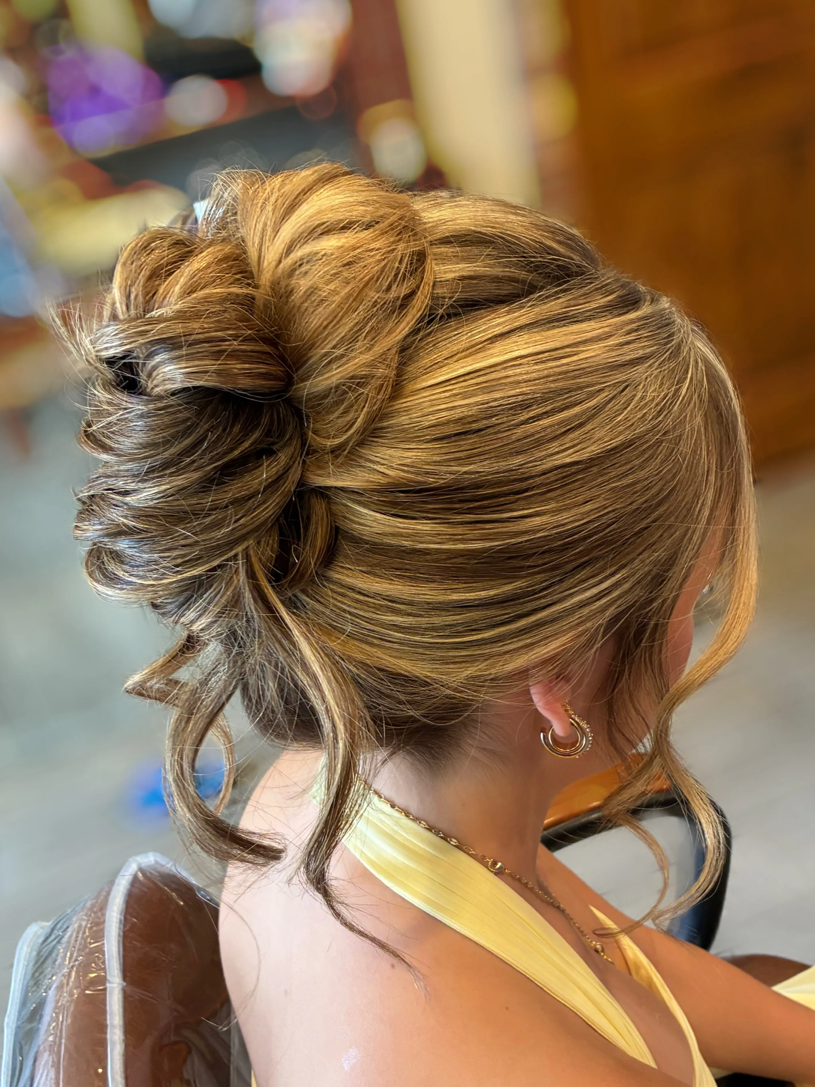 Sculpted blonde knotted high bun with smooth sides and curled tendrils