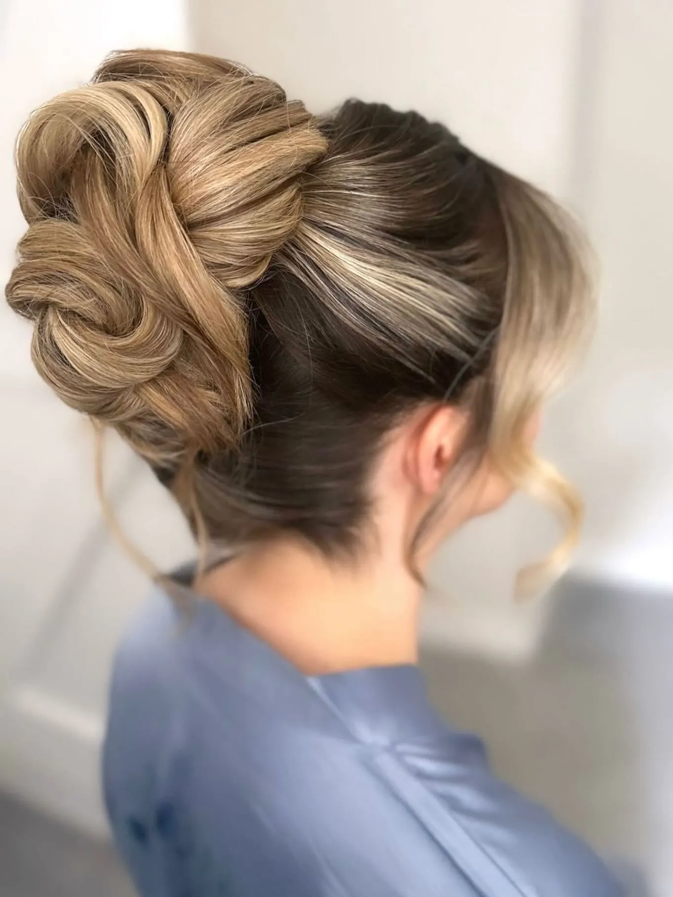 Smooth blonde looped high bun with a sleek crown and soft front curl