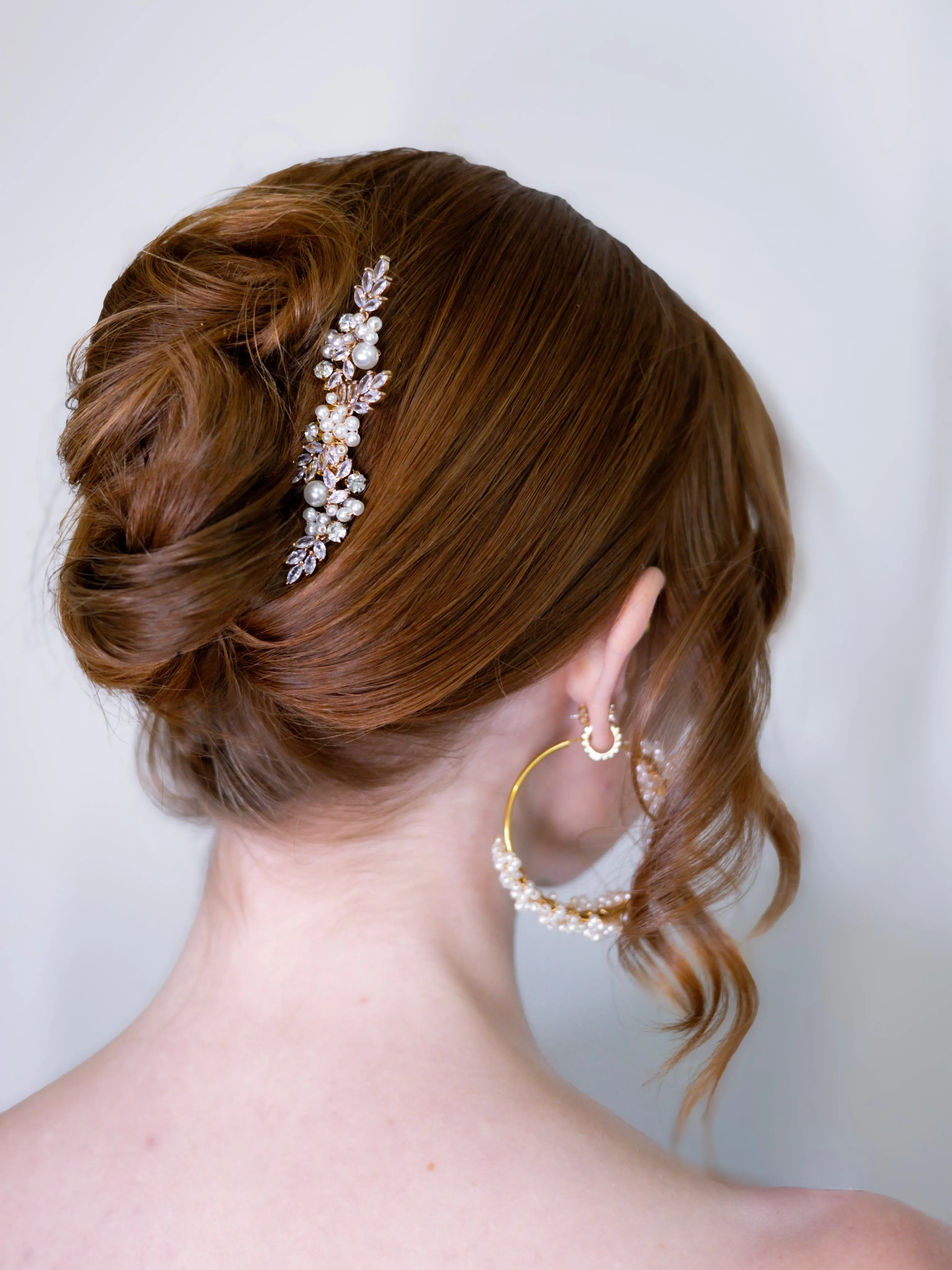 Sleek side wedding bun with a crystal barrette and curled face-framing piece