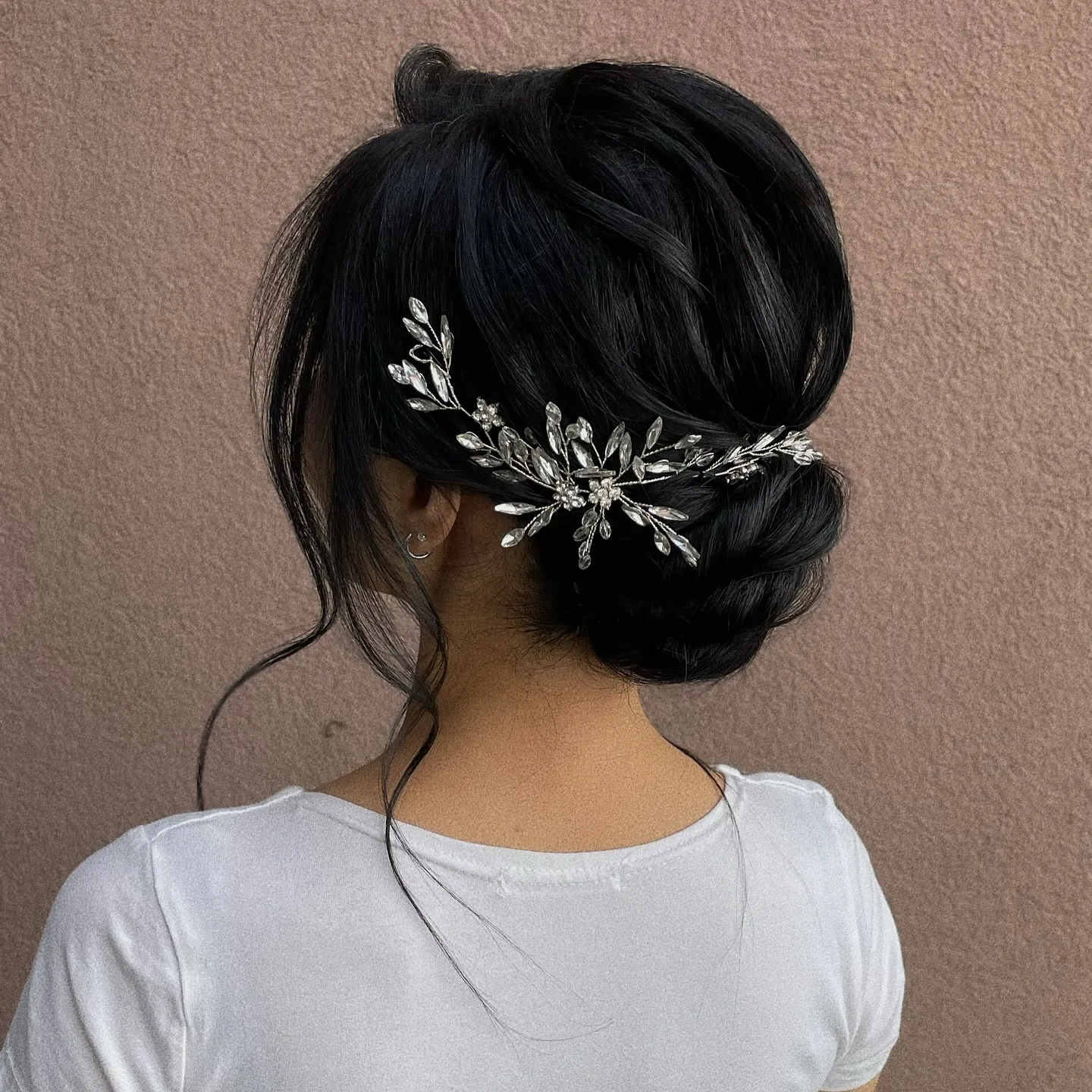 Low wedding bun with smooth crown, loose tendrils and a silver leaf hair vine