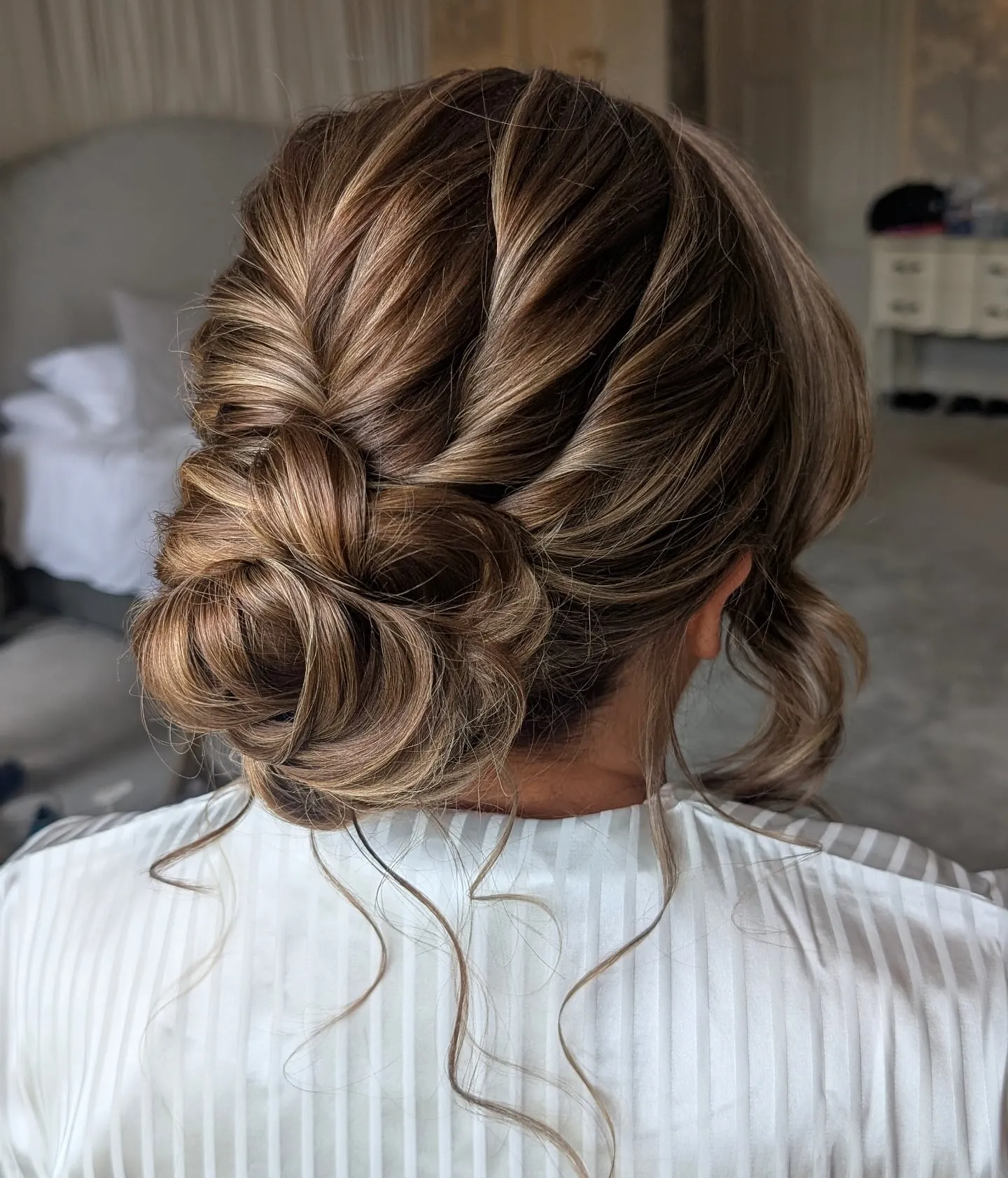 Twisted low wedding bun with broad side sections and loose curled tendrils