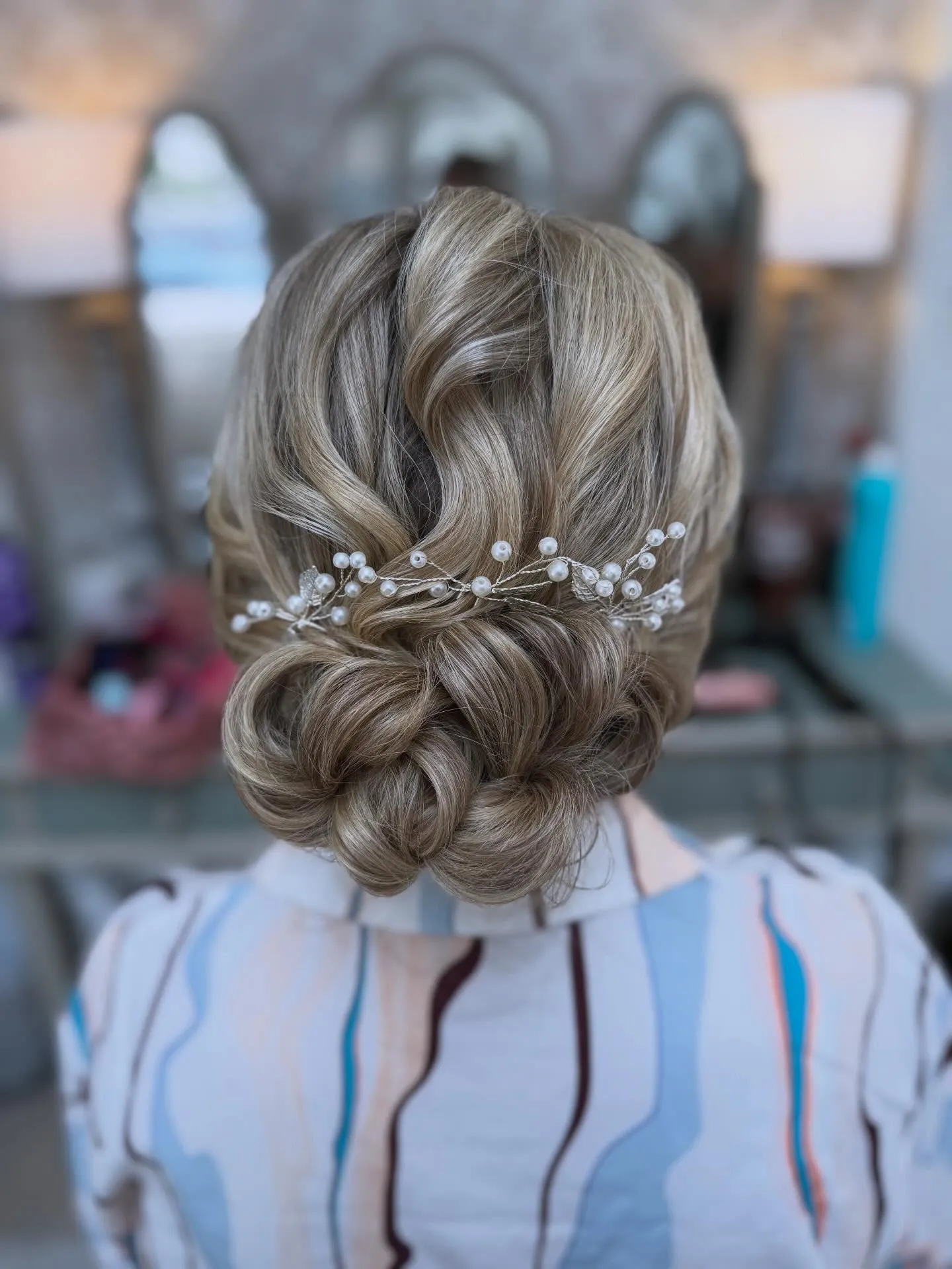 Rounded low wedding bun with soft twists and a pearl vine across the back