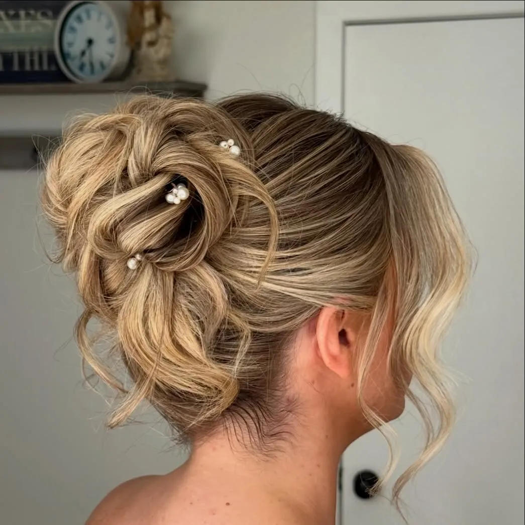 Tousled high wedding bun with curled loops, loose tendrils and scattered pearl pins