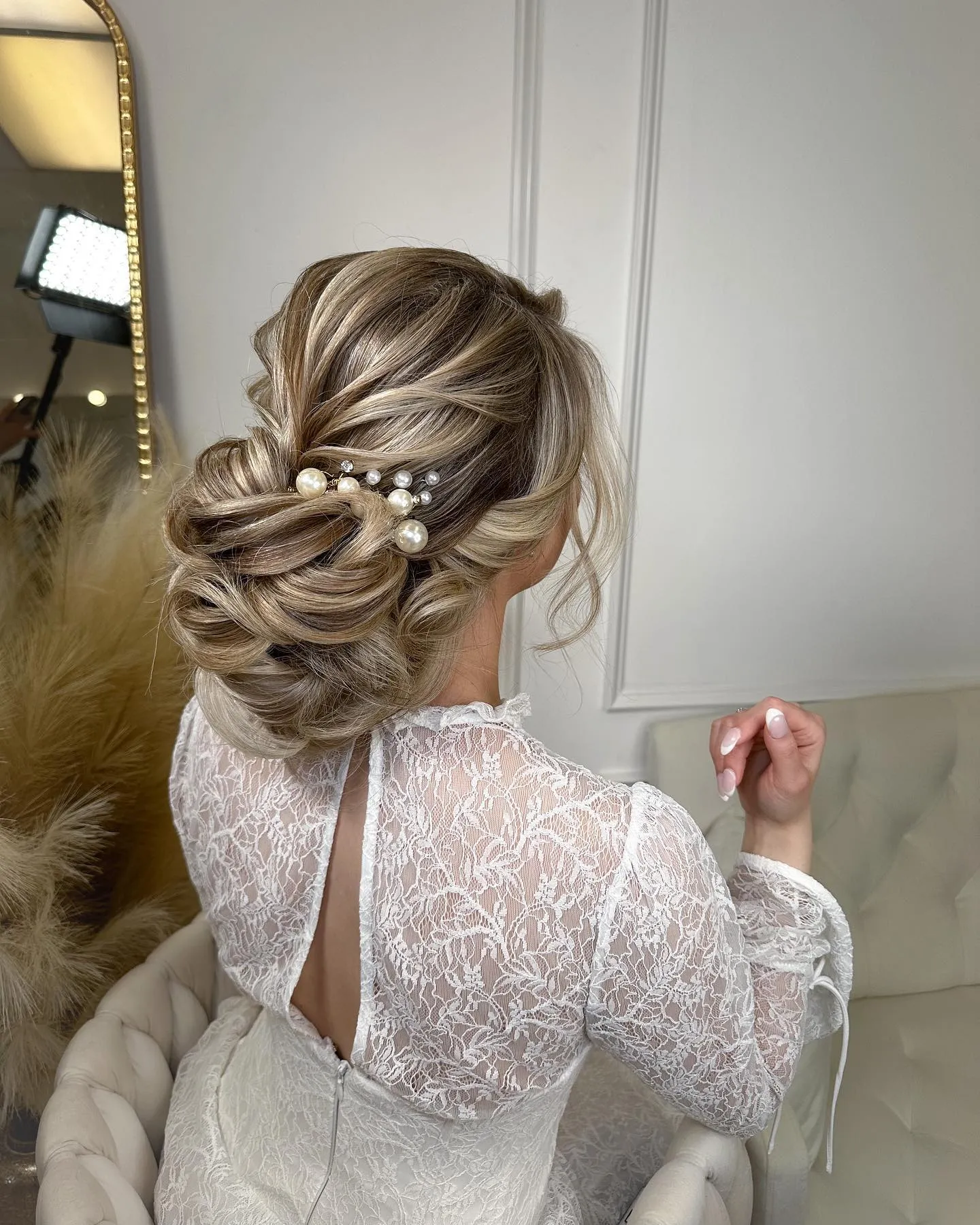 Textured low wedding bun with sweeping sections, loose tendrils and pearl pins