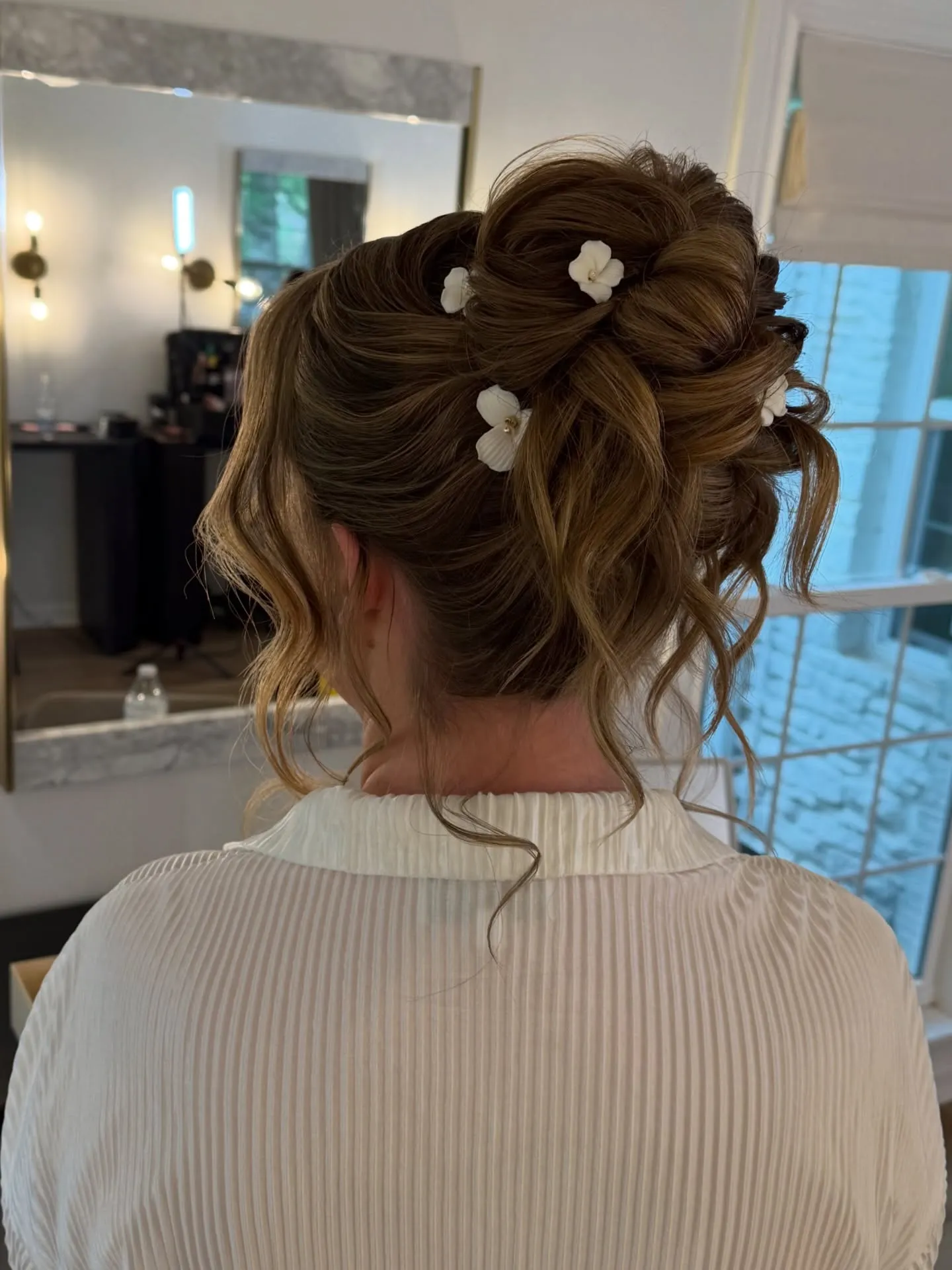 Romantic curled wedding updo with soft loops, loose tendrils and small flower pins
