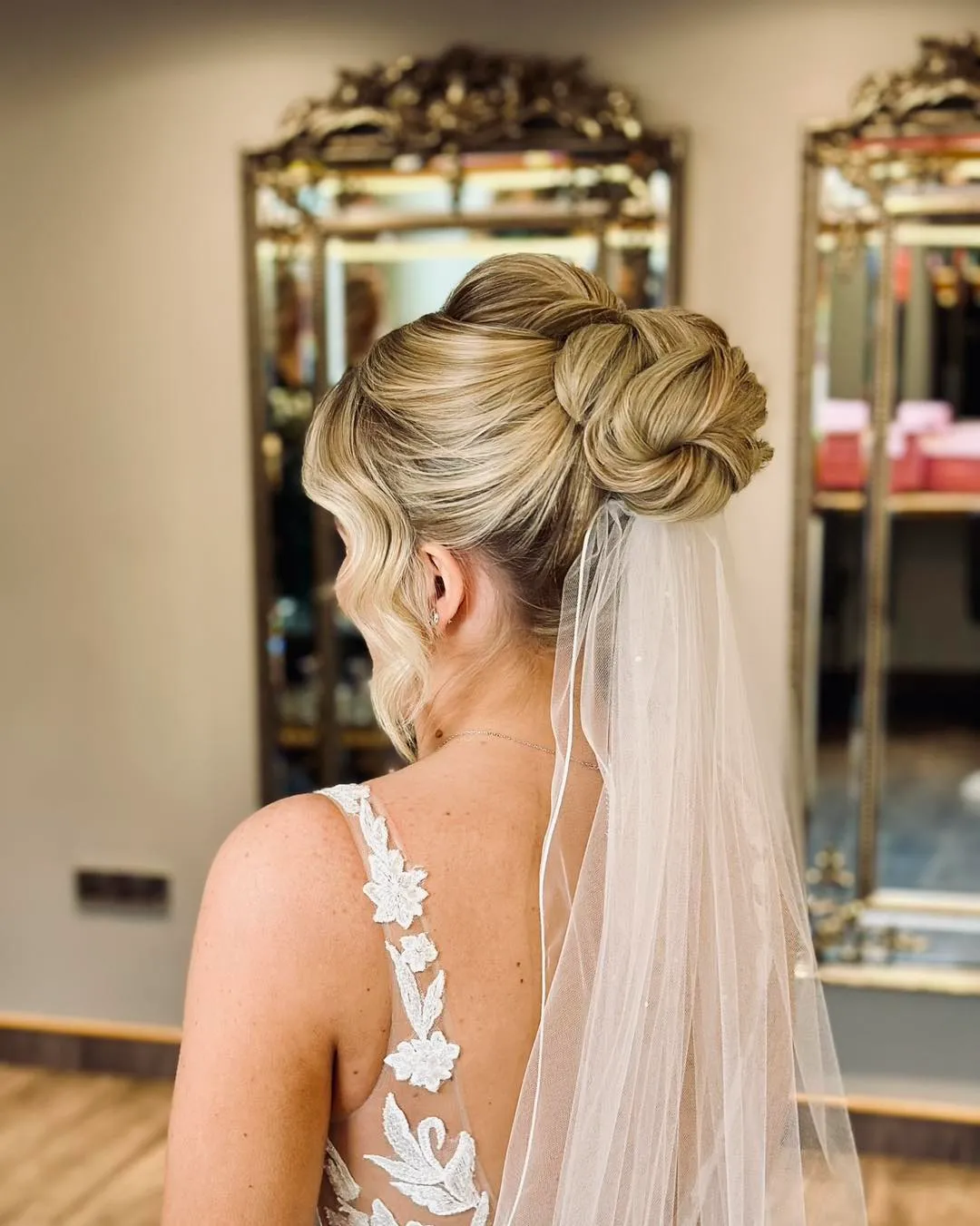 High rosette wedding bun with a smooth crown, loose front wave and veil underneath