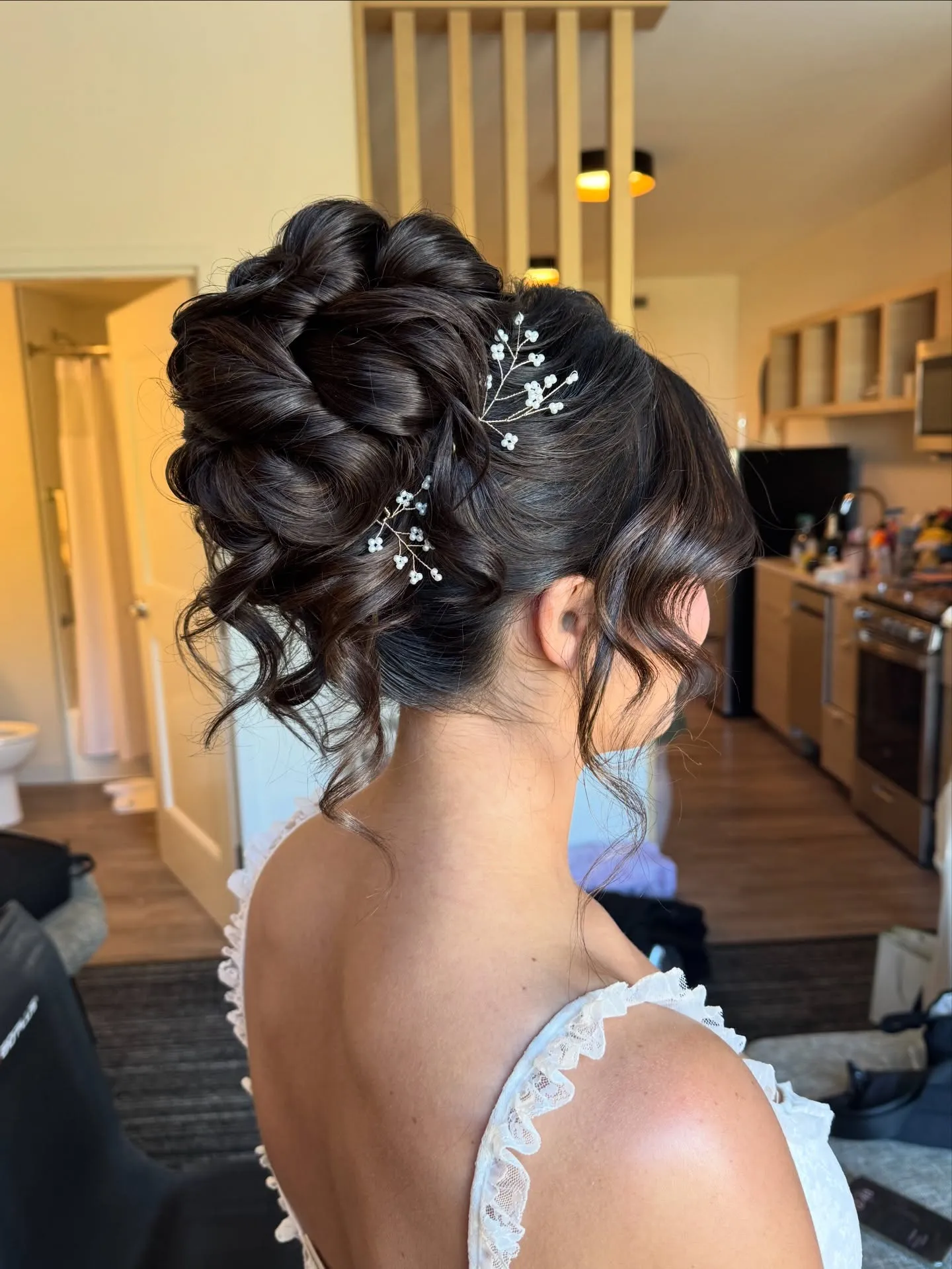 High braided wedding bun with glossy loops, floral pins and curled face-framing pieces
