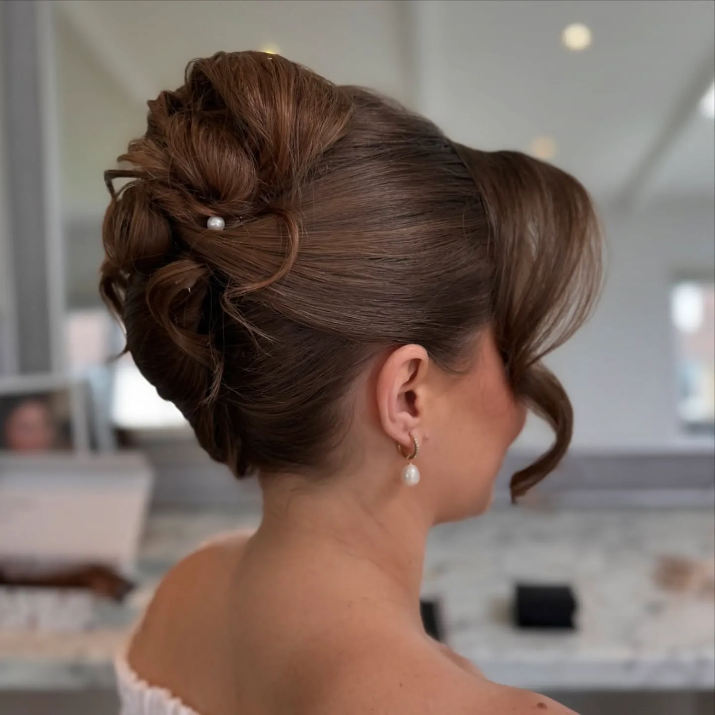 Sleek French roll wedding updo with sculpted loops, side fringe and a pearl pin