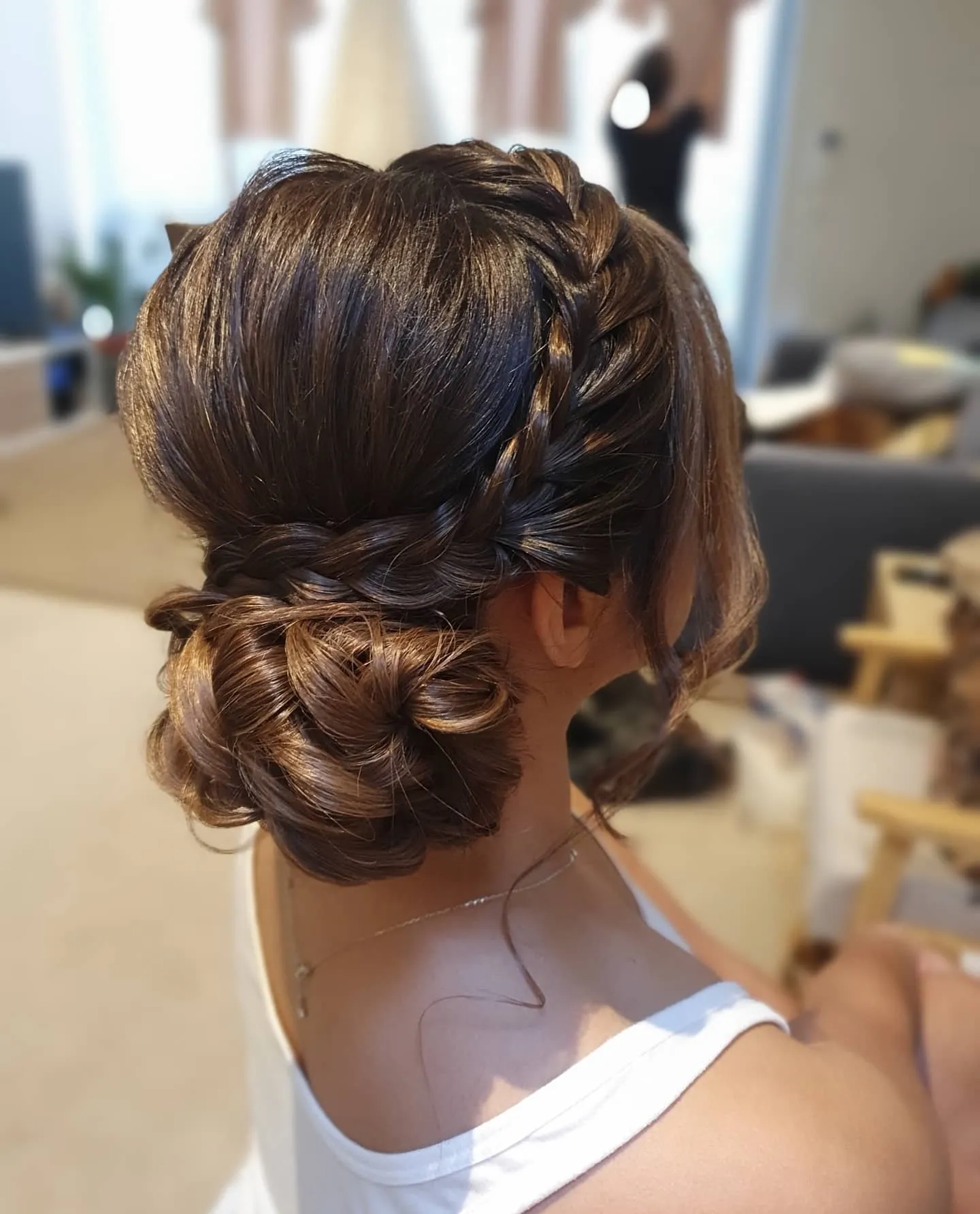 Side-braided low wedding bun with a smooth crown and loose face-framing tendril