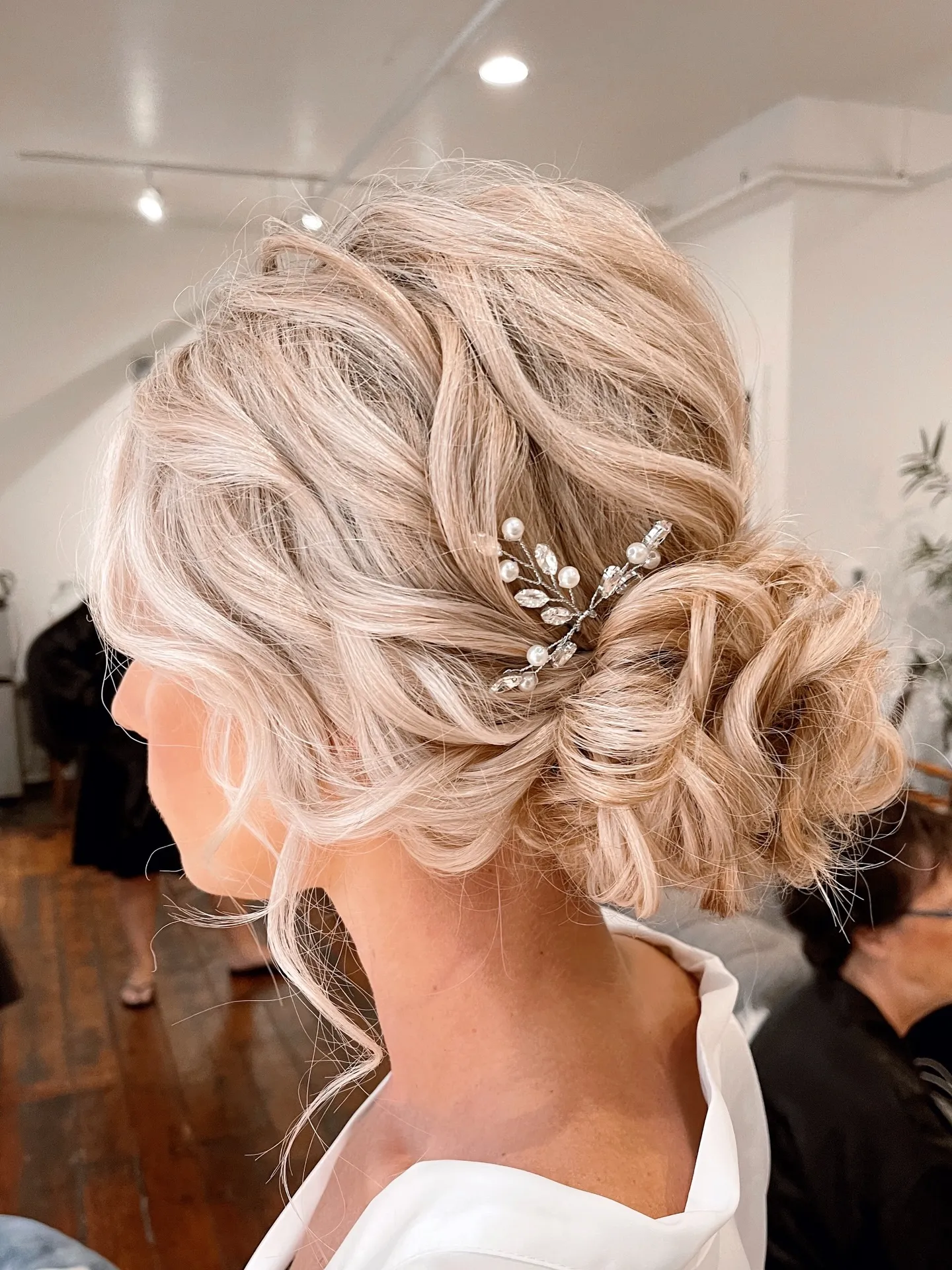 Soft low wedding bun with airy curls, loose tendrils and a pearl sprig