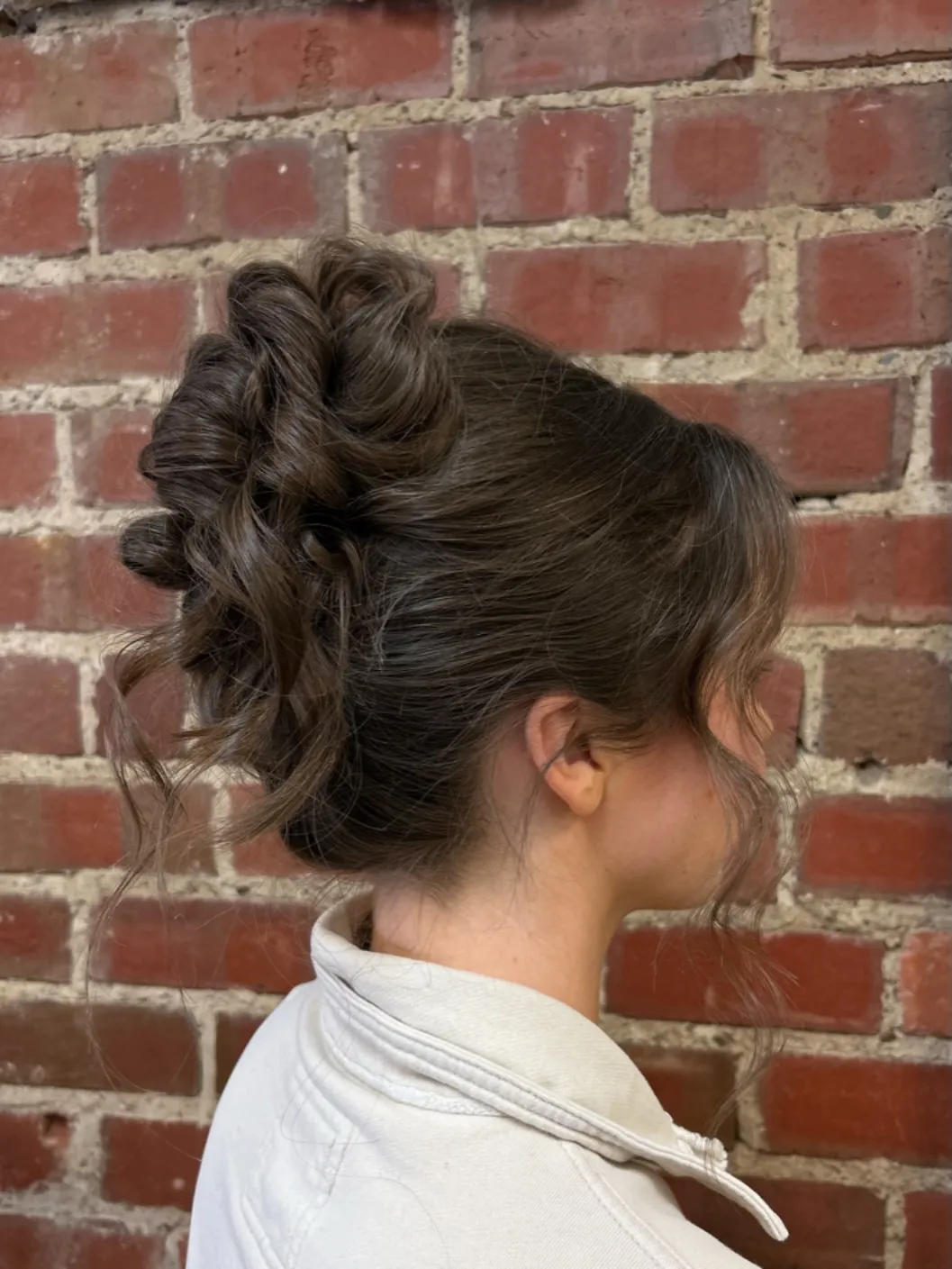 Textured high wedding updo with stacked loops and loose curled tendrils