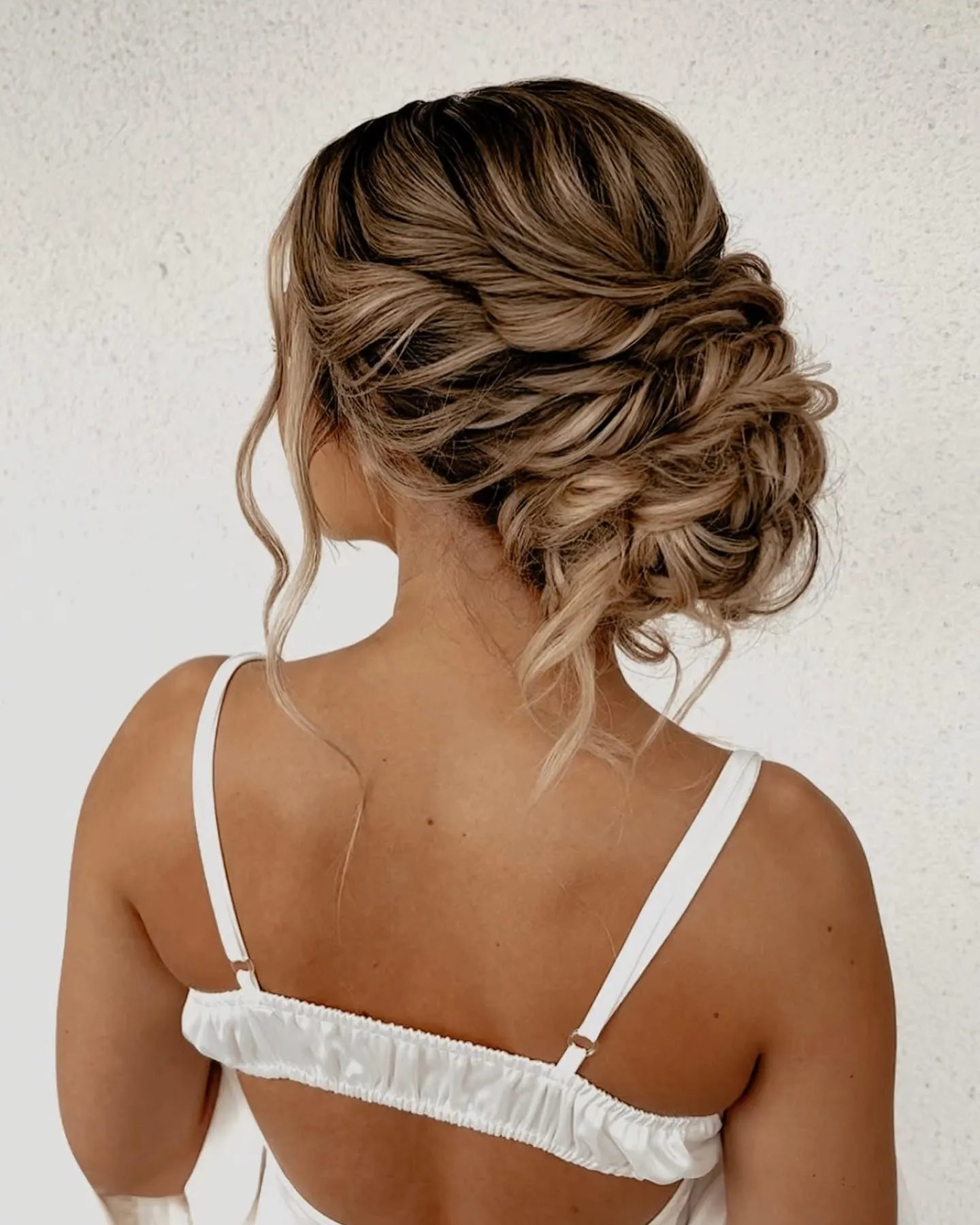 Twisted low wedding bun with swept side sections and loose curled tendrils