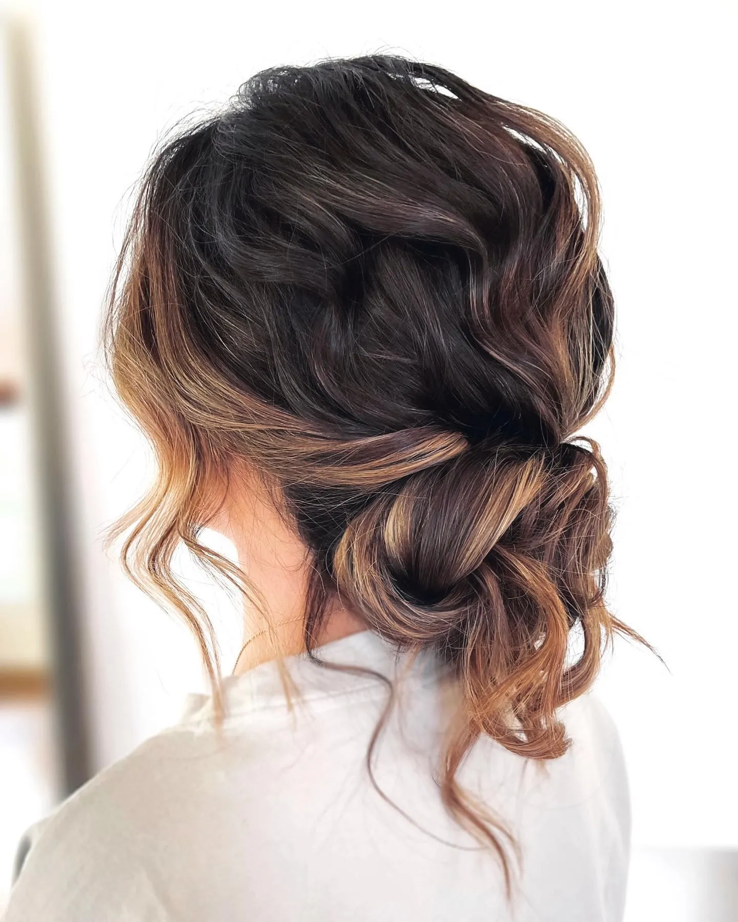 Soft low messy bun on dark brown hair with warm curled ends