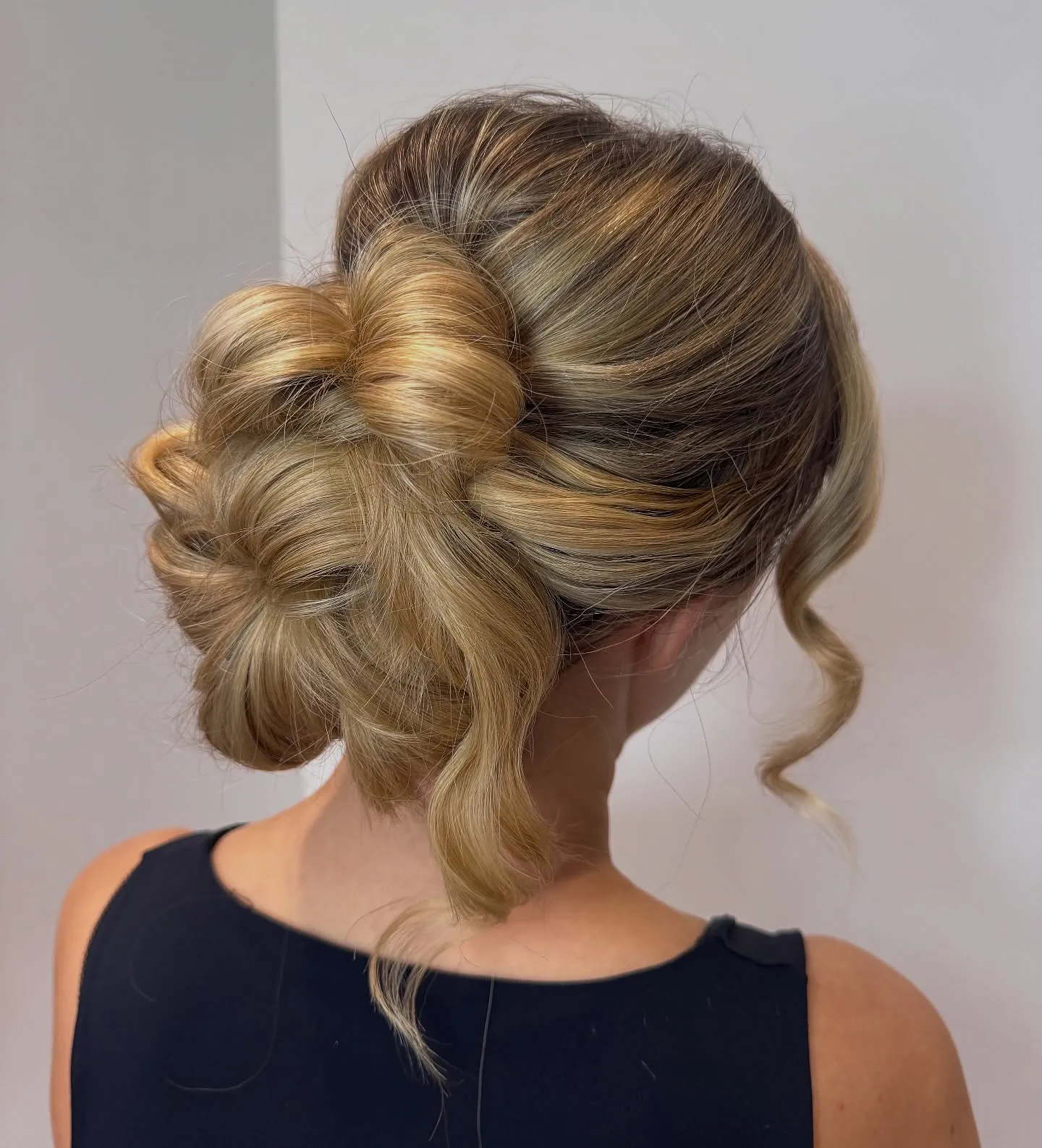 Rounded low blonde bun with sculpted loops and side sweep