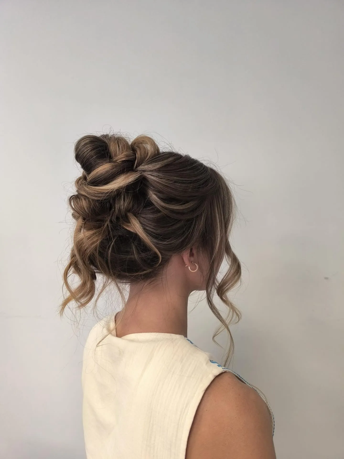 High looped messy bun on brown hair with curled tendrils