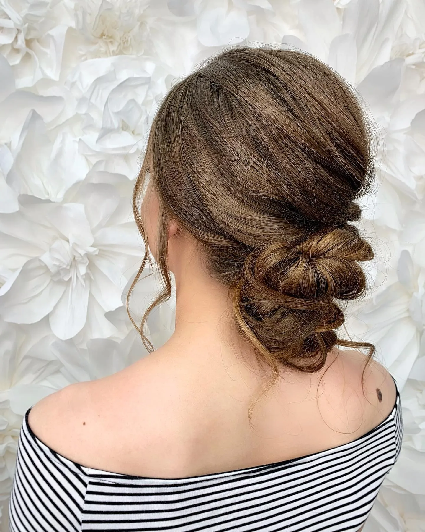 Knotted low bun on brown hair with a loose curled tendril