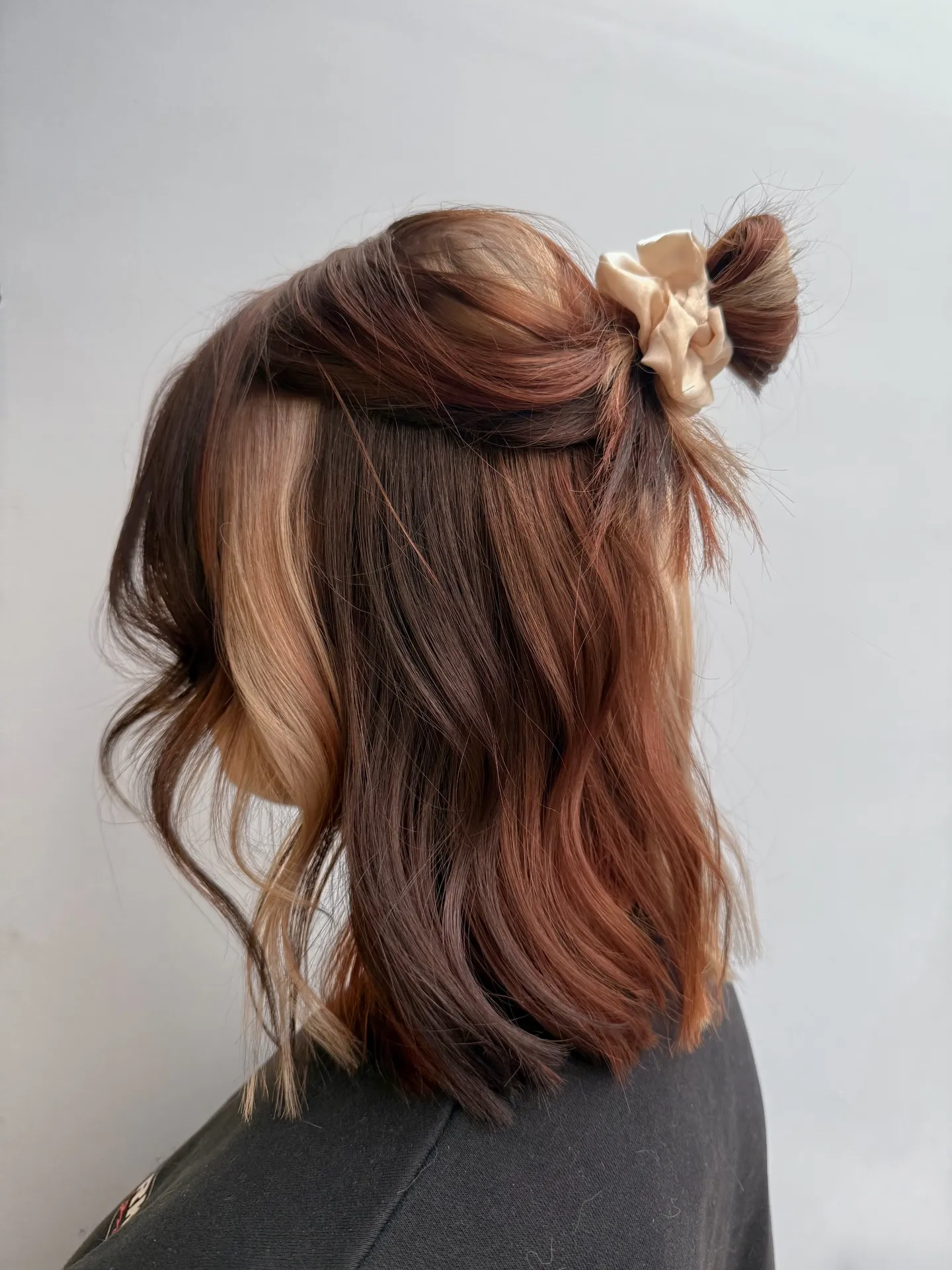 Wavy shoulder-length lob with a small half-up bun and face-framing pieces
