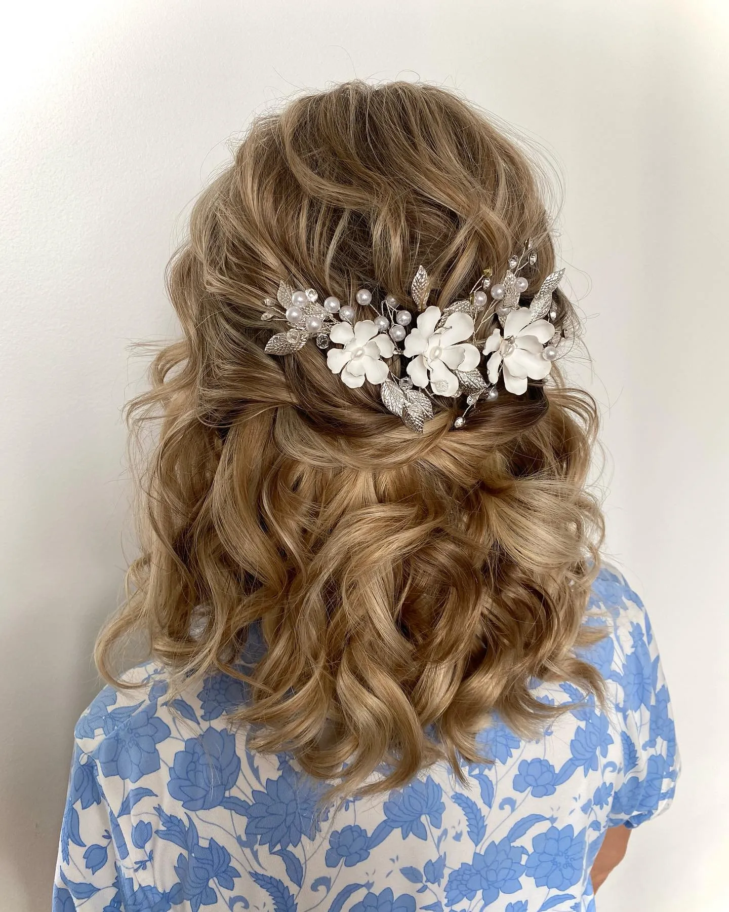 Blonde half-up curls with a white floral hairpiece