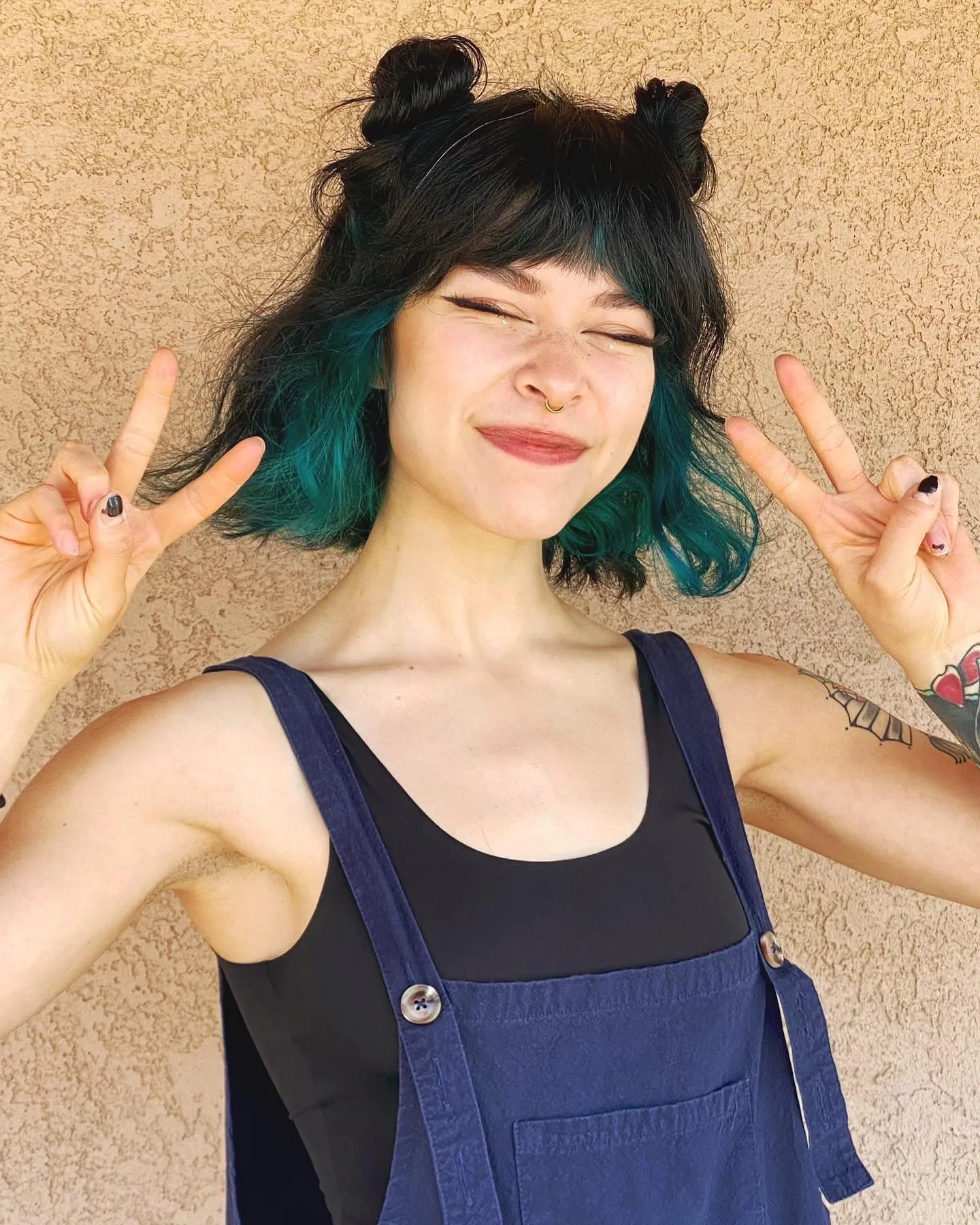 Dark razor cut bob with short fringe, teal ends, and small space buns