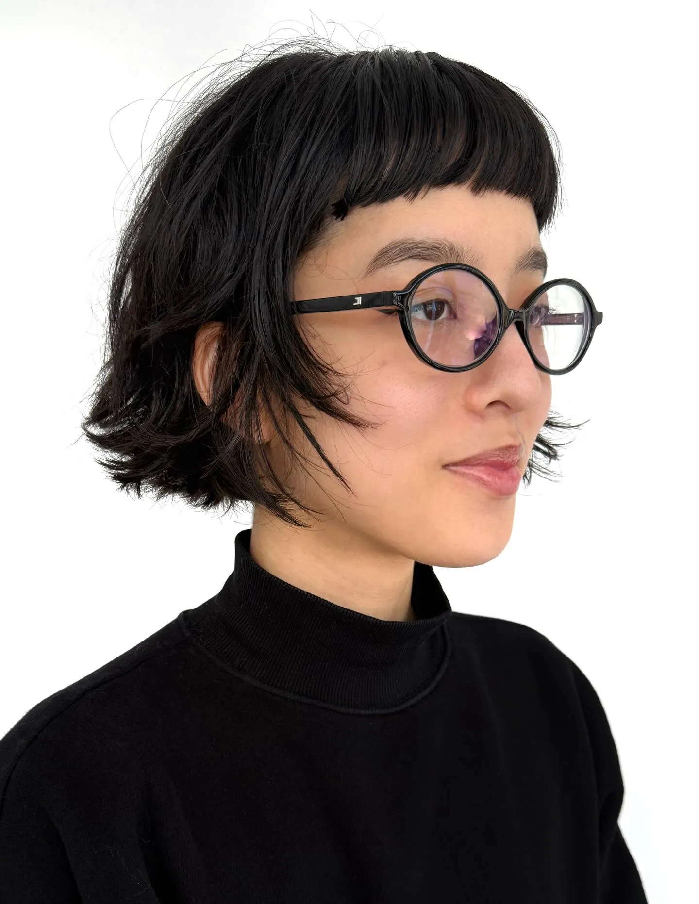 Short black bob with blunt micro fringe, flipped ends, and round glasses