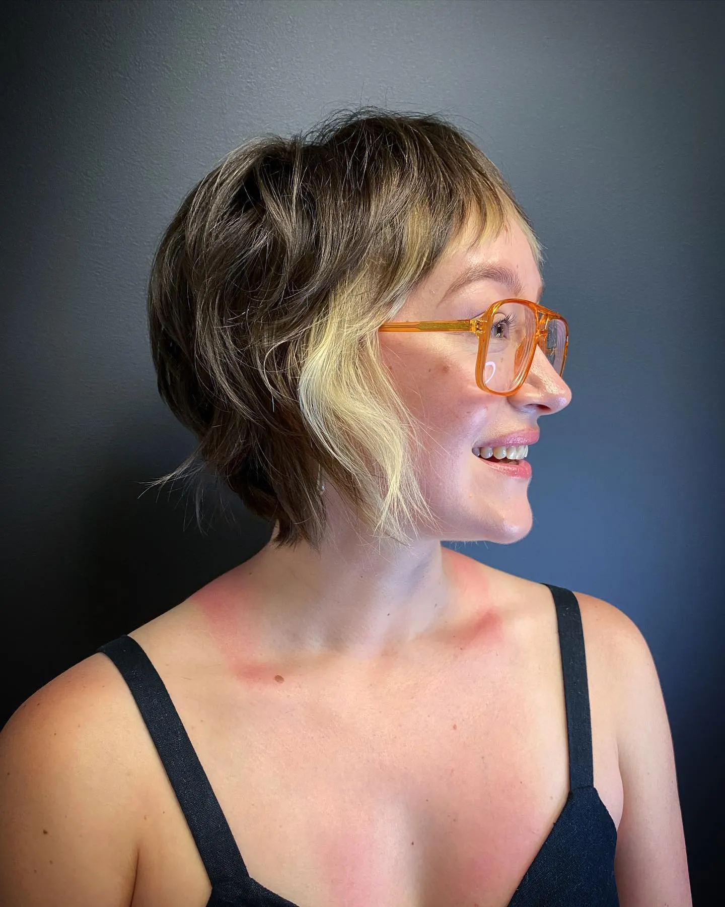 Tousled pixie bob with blonde face-framing pieces and amber glasses